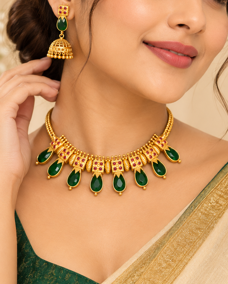 A woman wearing a gold and green traditional jewelry set, featuring a gold necklace with emerald-cut green stones and matching gold and green jhumka earrings, styled with a beige and green saree.