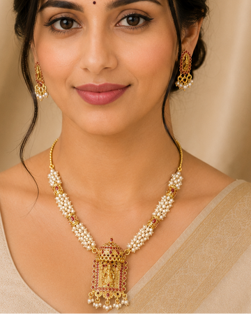 A woman wearing a gold and cream jewelry set with a necklace and matching earrings, styled with a beige saree against a draped beige background.