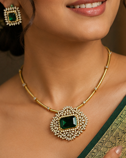 A woman wearing a dark green saree with a gold zari border and a matching gold necklace with a green stone pendant, photographed in a warm indoor setting.