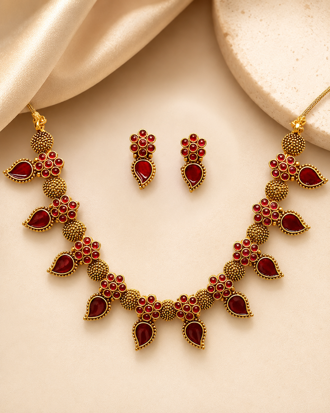 A woman wearing a gold and red traditional Indian jewelry set, featuring a necklace and matching earrings, styled with a beige sari.