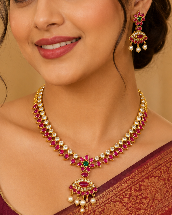 A woman wearing a traditional Indian outfit in deep maroon and gold, styled with a matching maroon blouse and a gold and red beaded necklace with matching earrings.