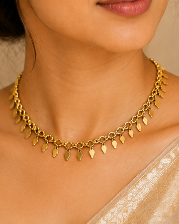 A woman wearing a gold leaf choker necklace and matching gold stud earrings, paired with a shimmering champagne-colored blouse.