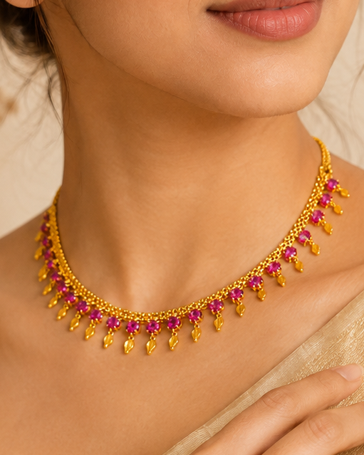 A woman wearing a gold-toned choker necklace with red gemstone accents, styled with a beige sari against a soft beige background.