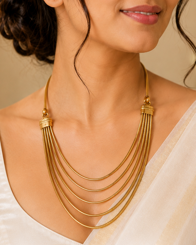 A woman wearing a multi-strand gold necklace with a layered, tiered design over a white sari, shown in a warm, elegant indoor setting.