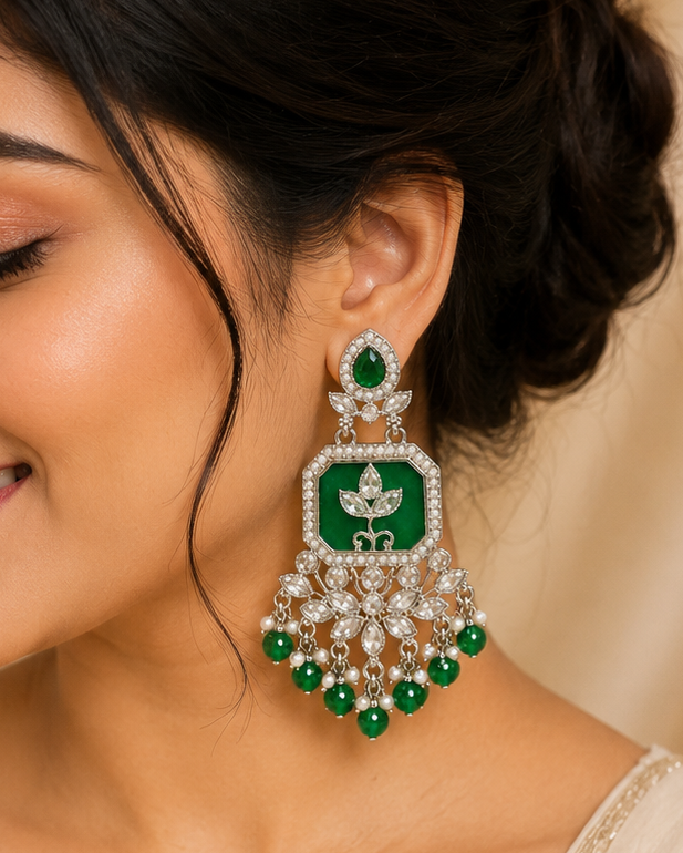 A woman wearing a large green and silver-toned traditional Indian jhumka earring, shown in a close-up portrait against a soft beige background.