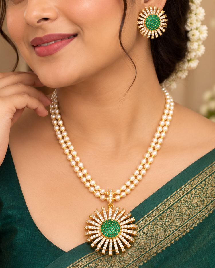 A woman wearing a green and gold traditional Indian sari with a matching gold and green statement necklace and earrings, posing in an elegant indoor setting.