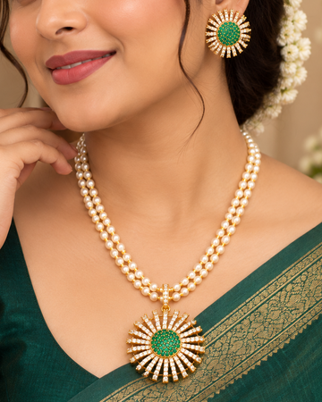 A woman wearing a green and gold traditional Indian sari with a matching gold and green statement necklace and earrings, posing in an elegant indoor setting.
