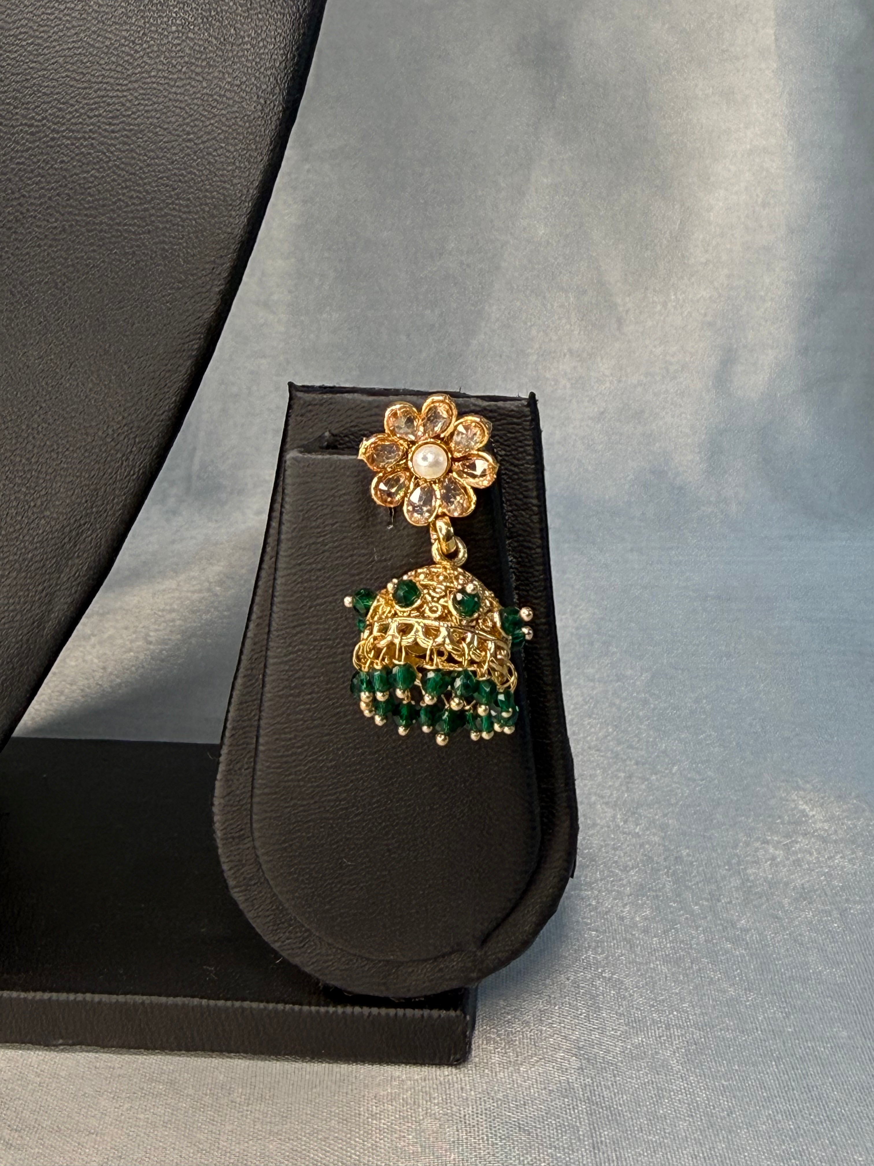 Gold and green decorative earring on a black stand against a gray background