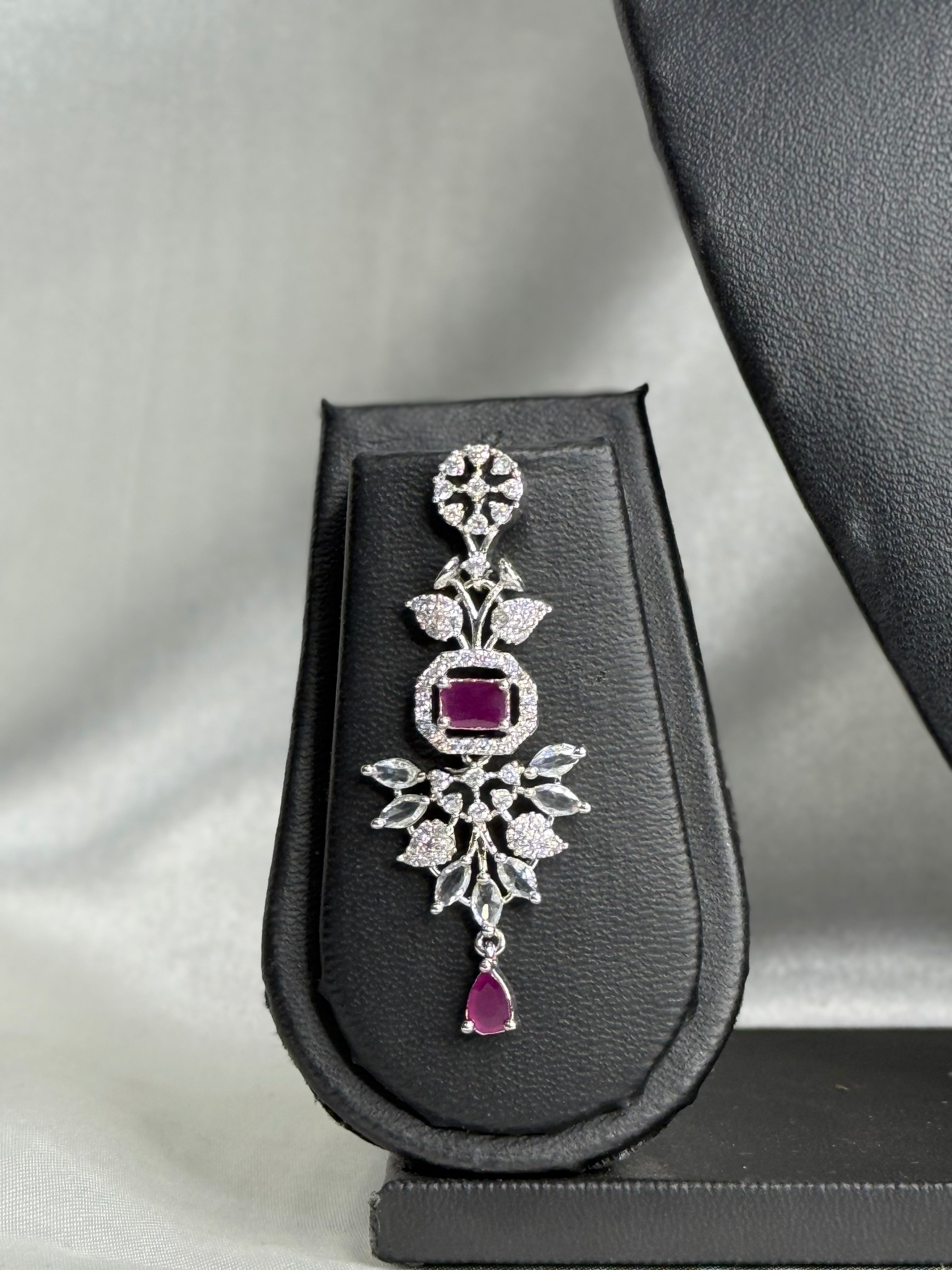 Silver pendant with purple gemstones on a gray stand