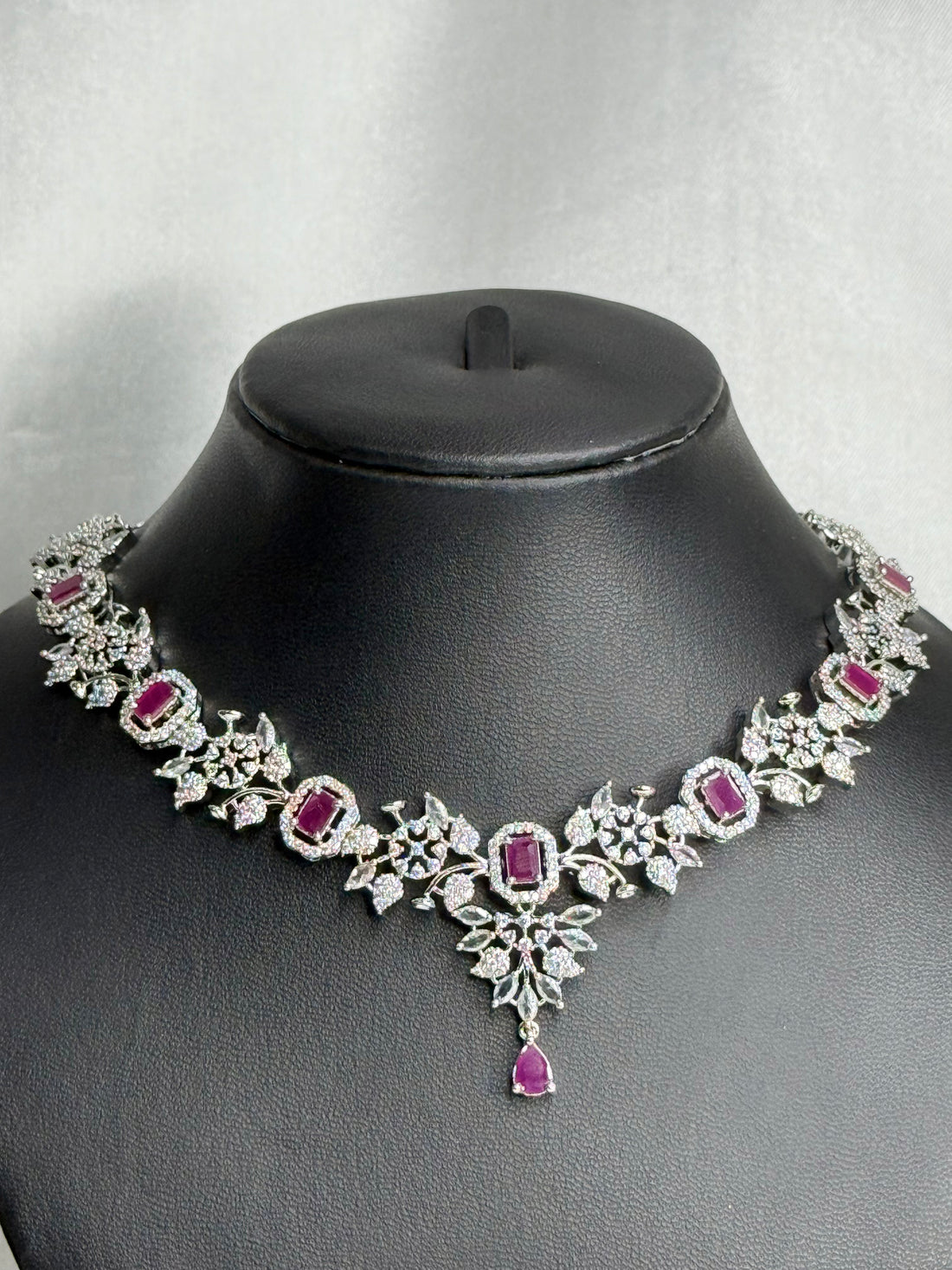 Jewelry set with necklace, earrings, and pouches on a black mannequin bust against a gray background.