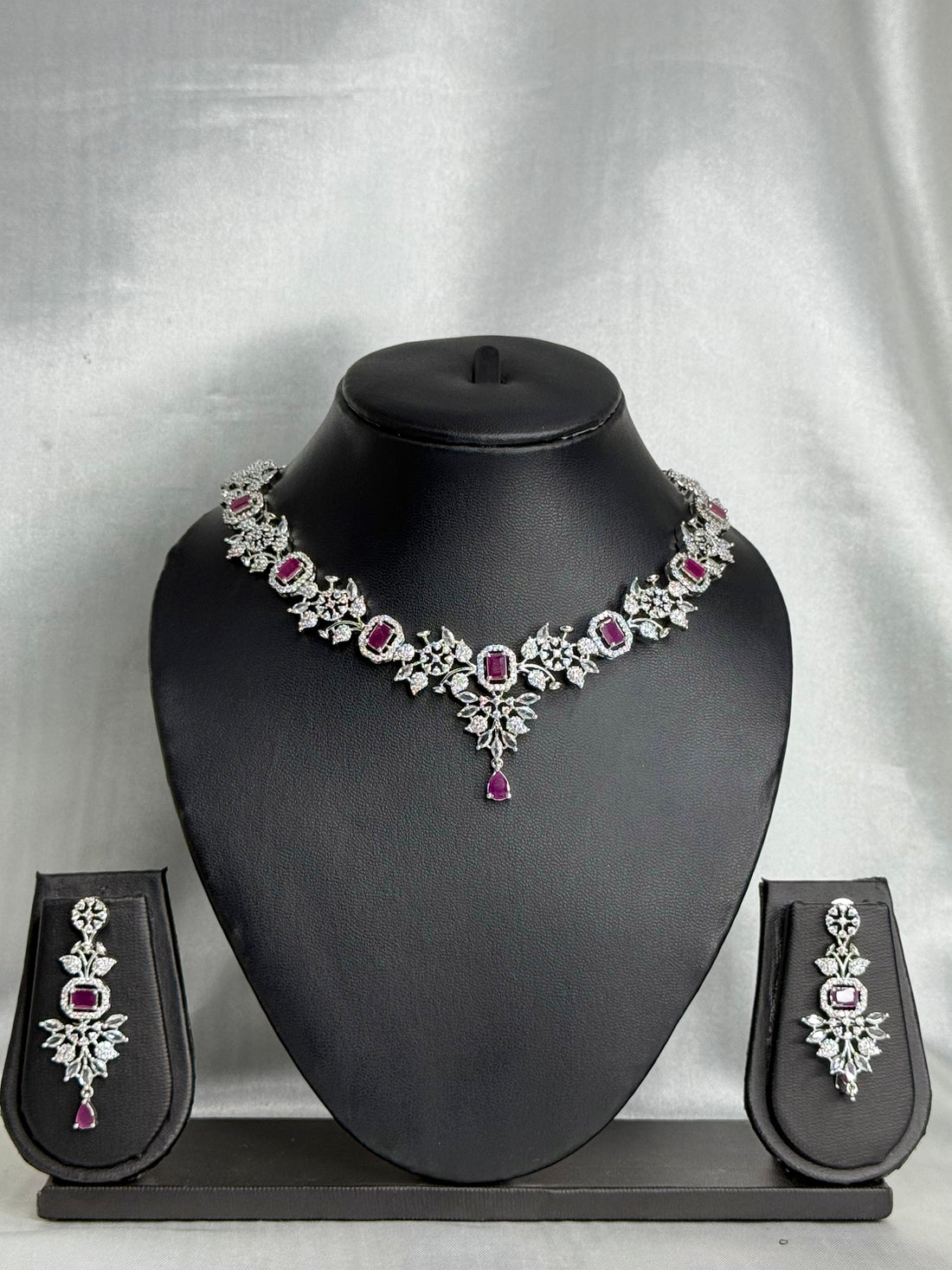 Jewelry set with necklace, earrings, and pouches on a black mannequin bust against a gray background.