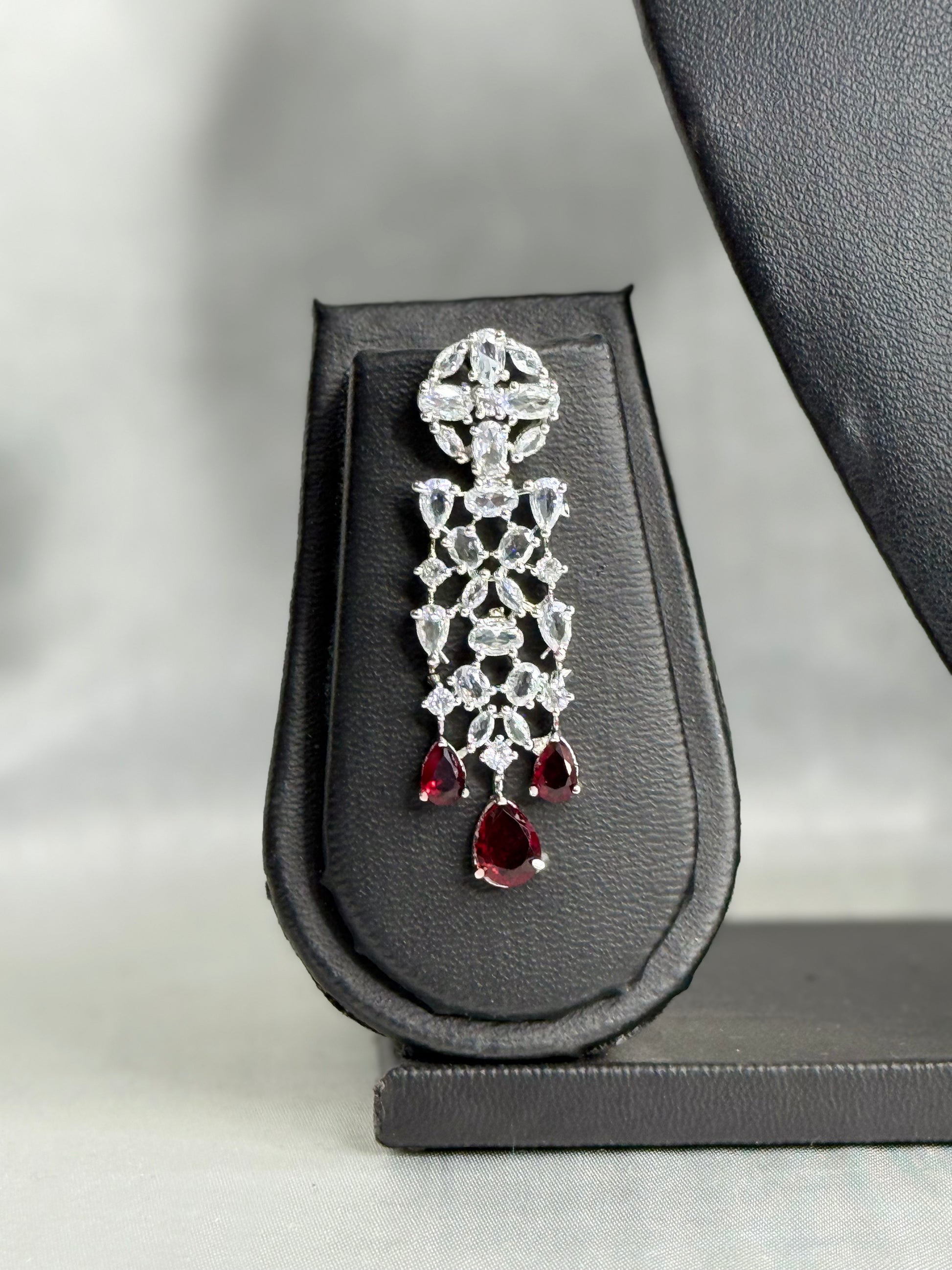 Diamond earring with red gemstones on a black stand