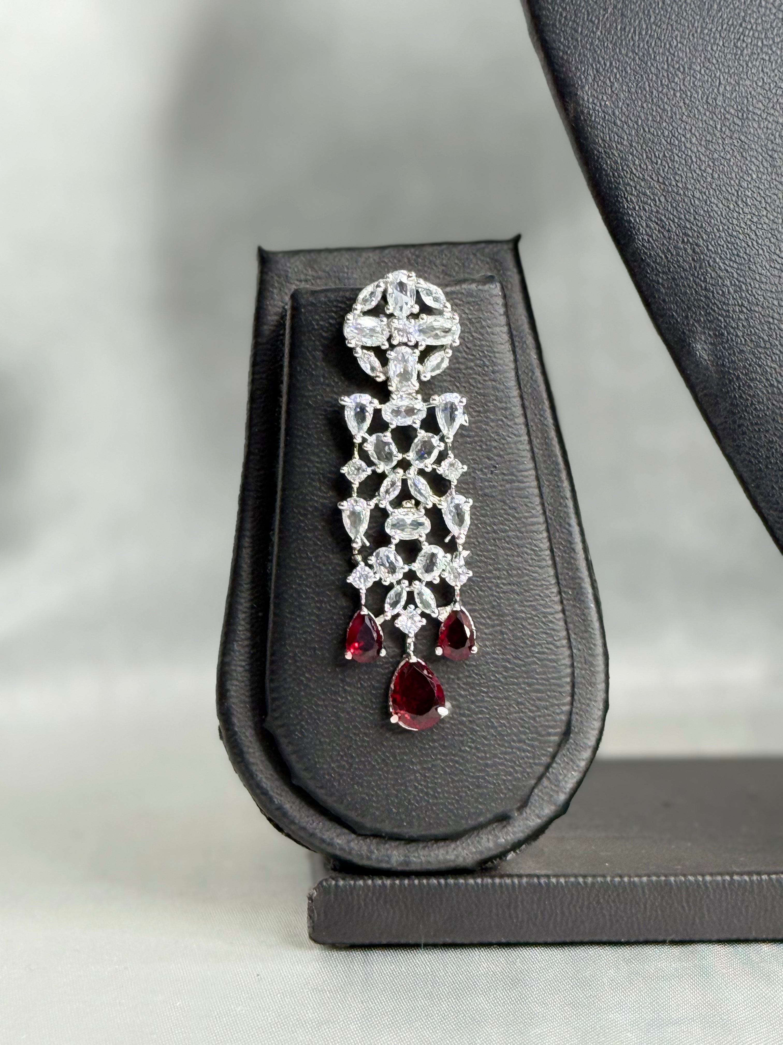 Diamond earring with red gemstones on a black stand