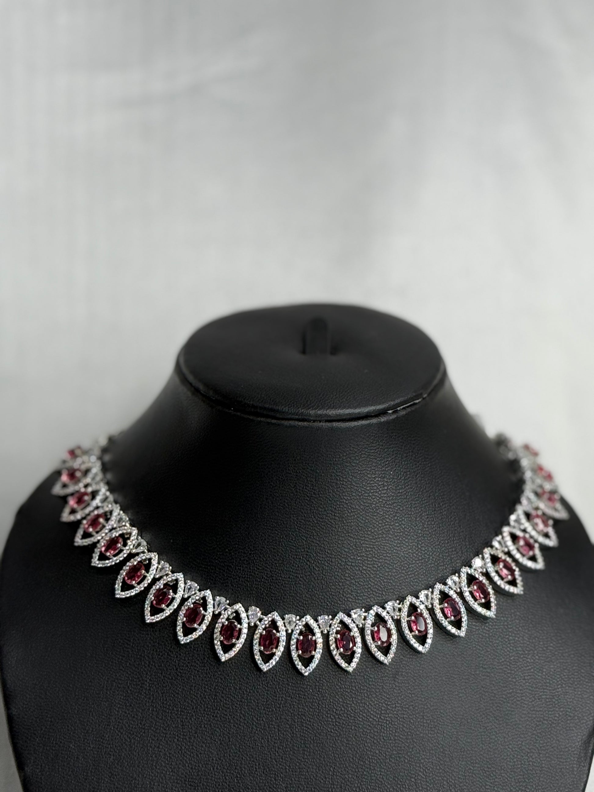 Necklace with red and clear stones on a black mannequin bust against a white background