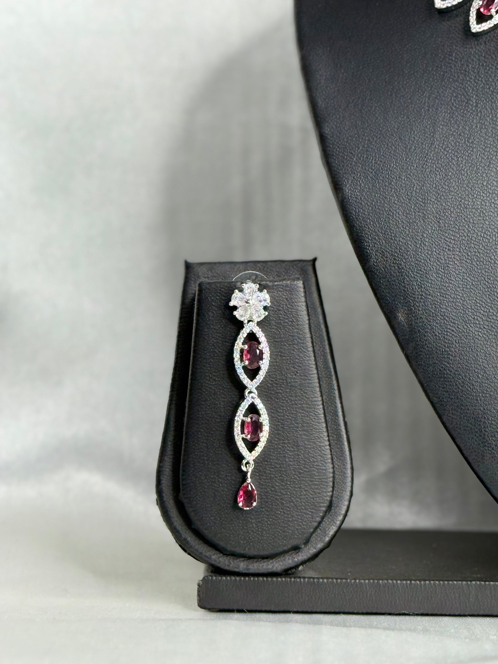 Silver earring with red gemstones on a black jewelry display stand.