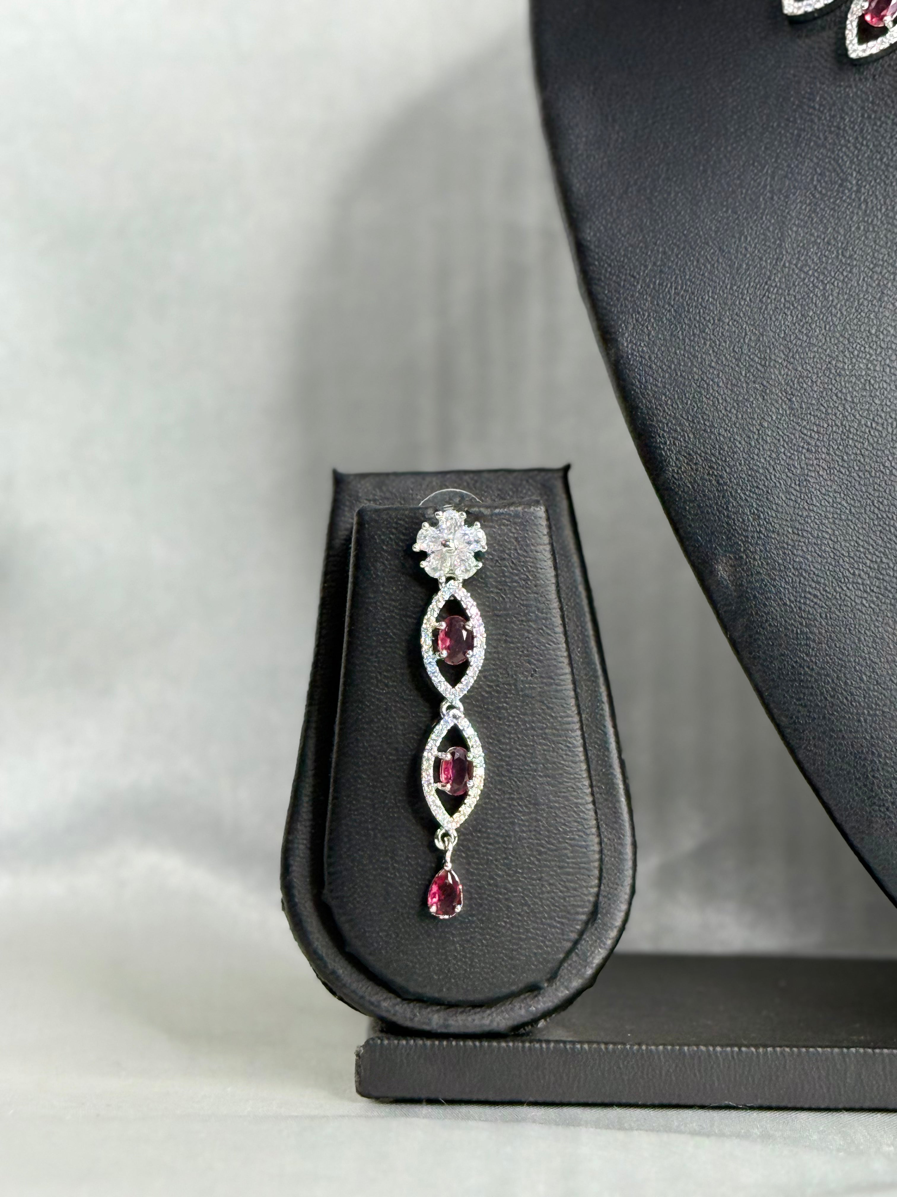 Silver earring with red gemstones on a black jewelry display stand.