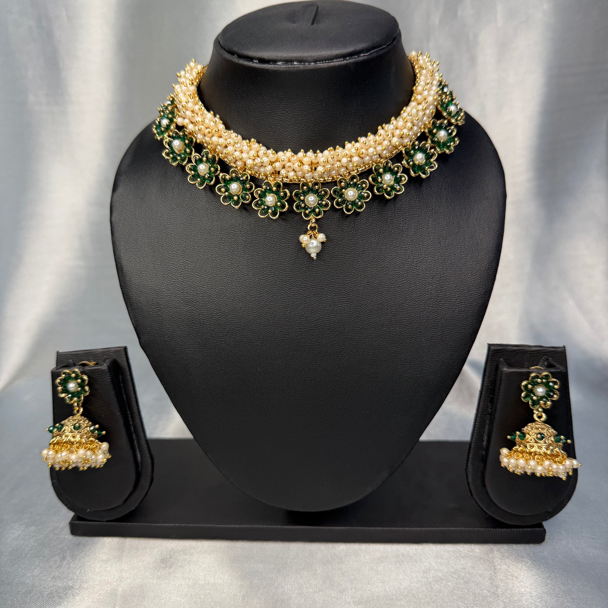 Pearl necklace with green gemstones and matching earrings on a black mannequin bust against a gray background.