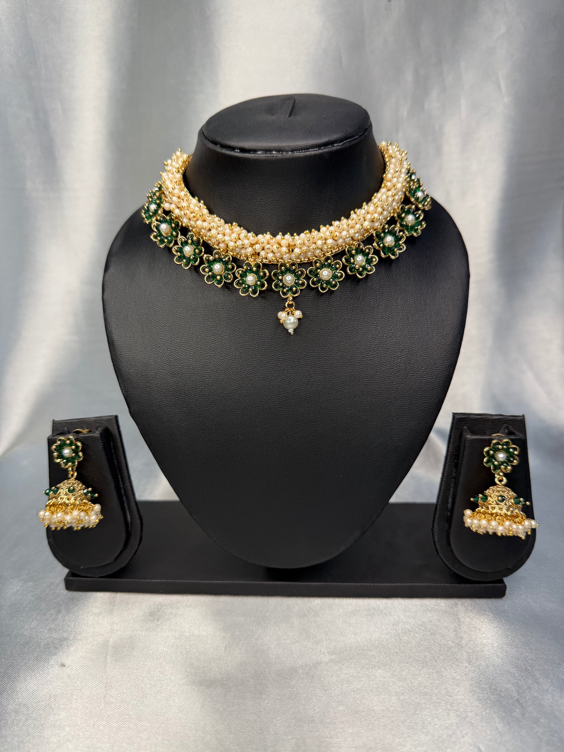 Pearl necklace with green gemstones and matching earrings on a black mannequin bust against a gray background.