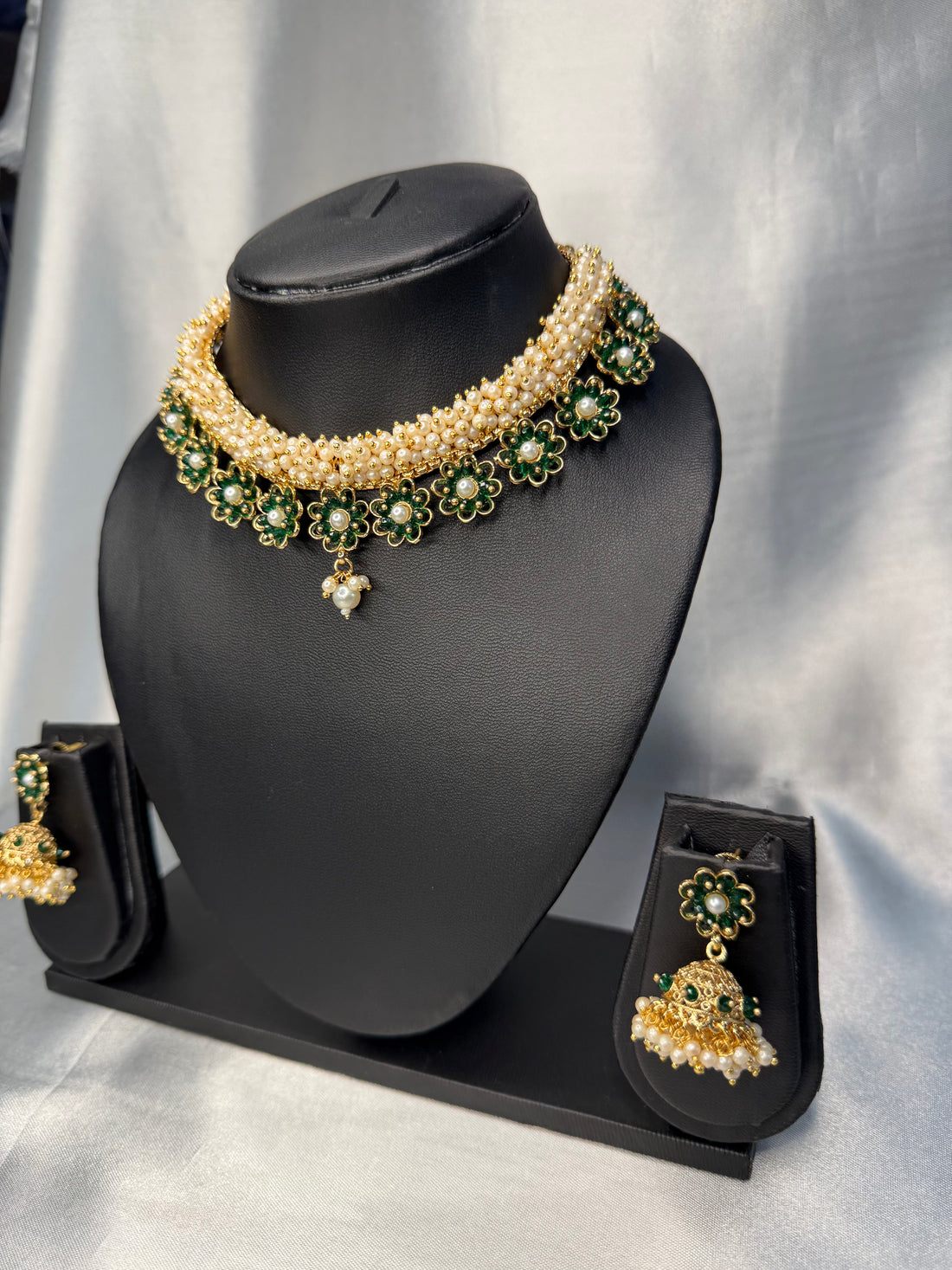 Pearl necklace with green gemstones and matching earrings on a black mannequin bust against a gray background.