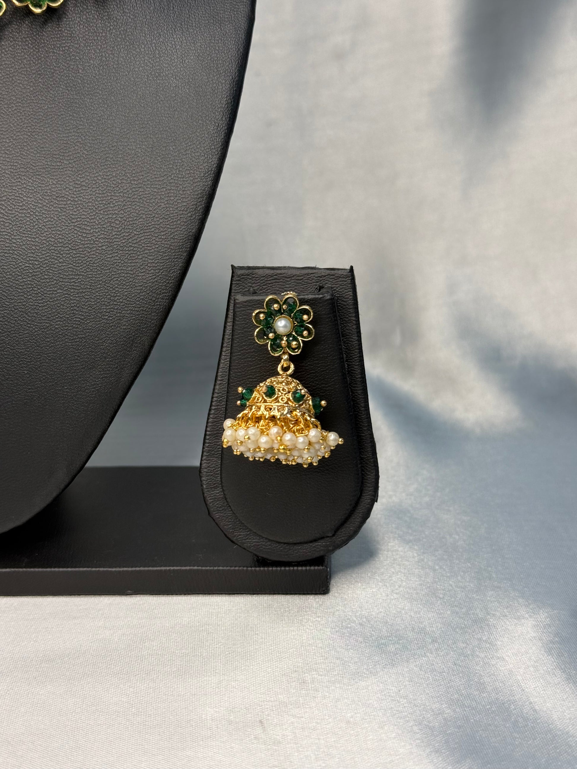 Gold and pearl earring on a black stand against a gray background