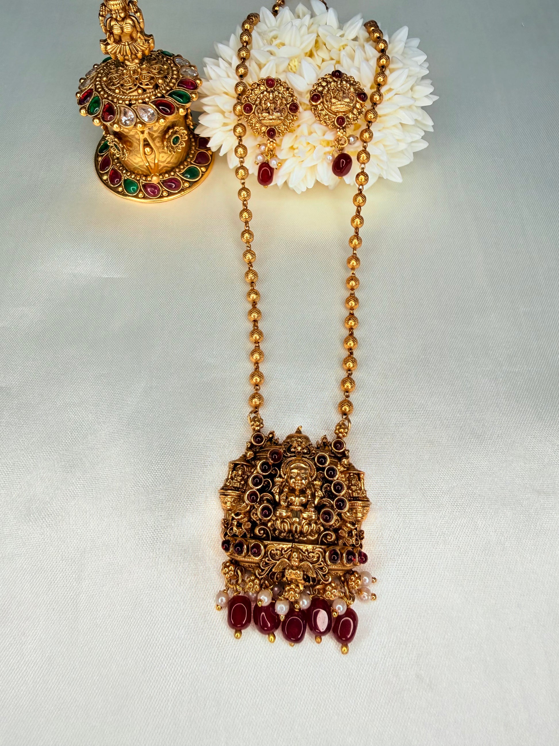 Ornate gold necklace with red gemstones and white flowers on a light gray background