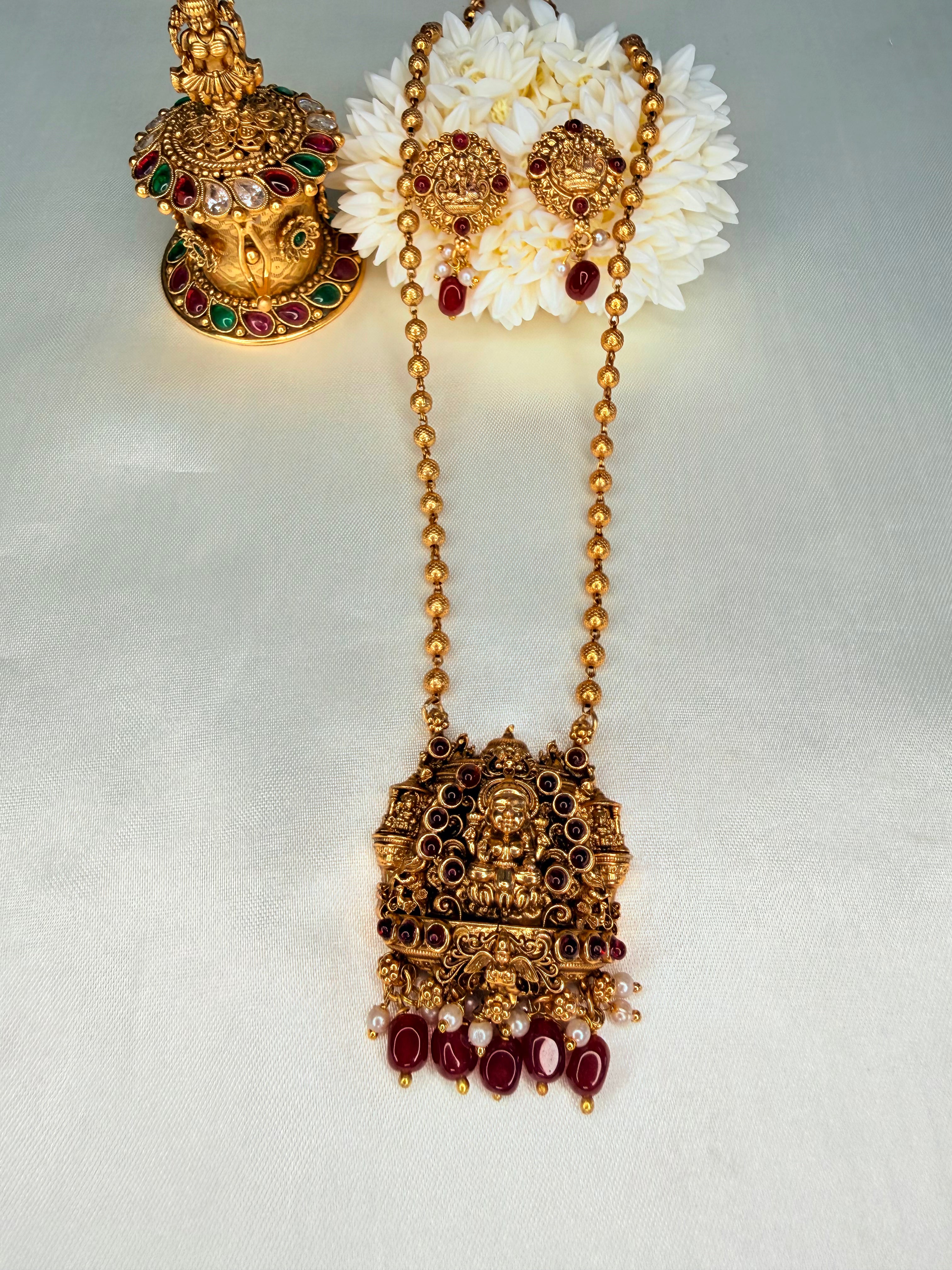 Ornate gold necklace with red gemstones and white flowers on a light gray background
