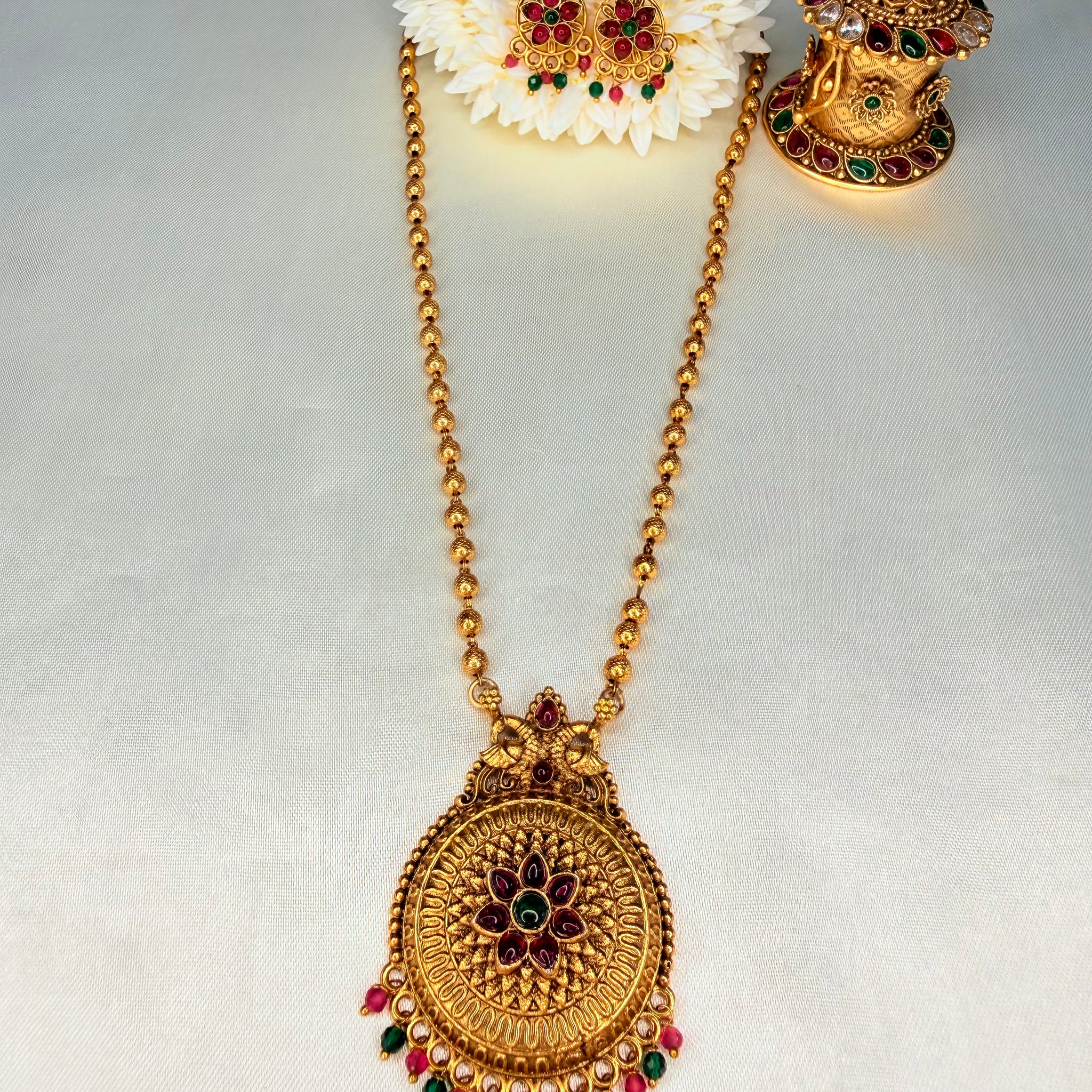 Gold necklace with floral hair accessory on a light gray background