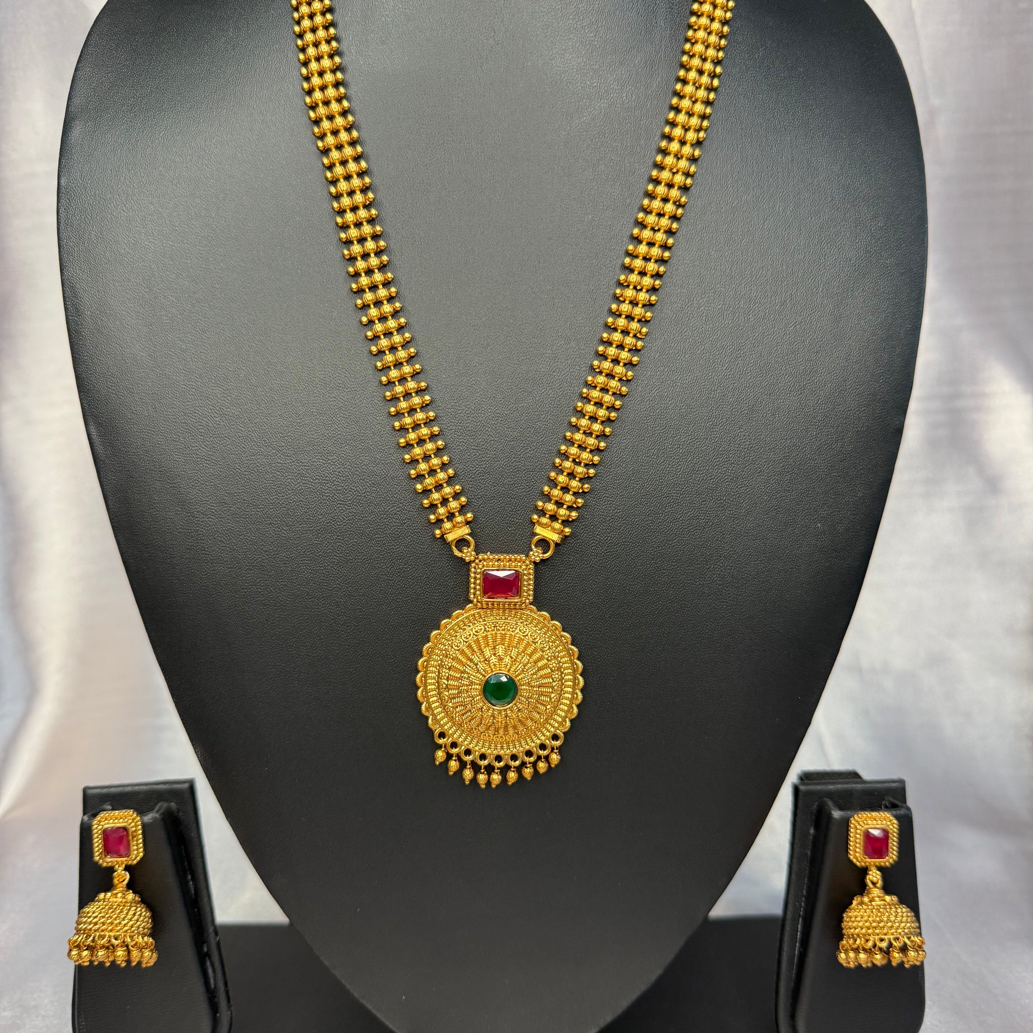 Gold necklace with pendant and earrings on a black mannequin bust against a white background