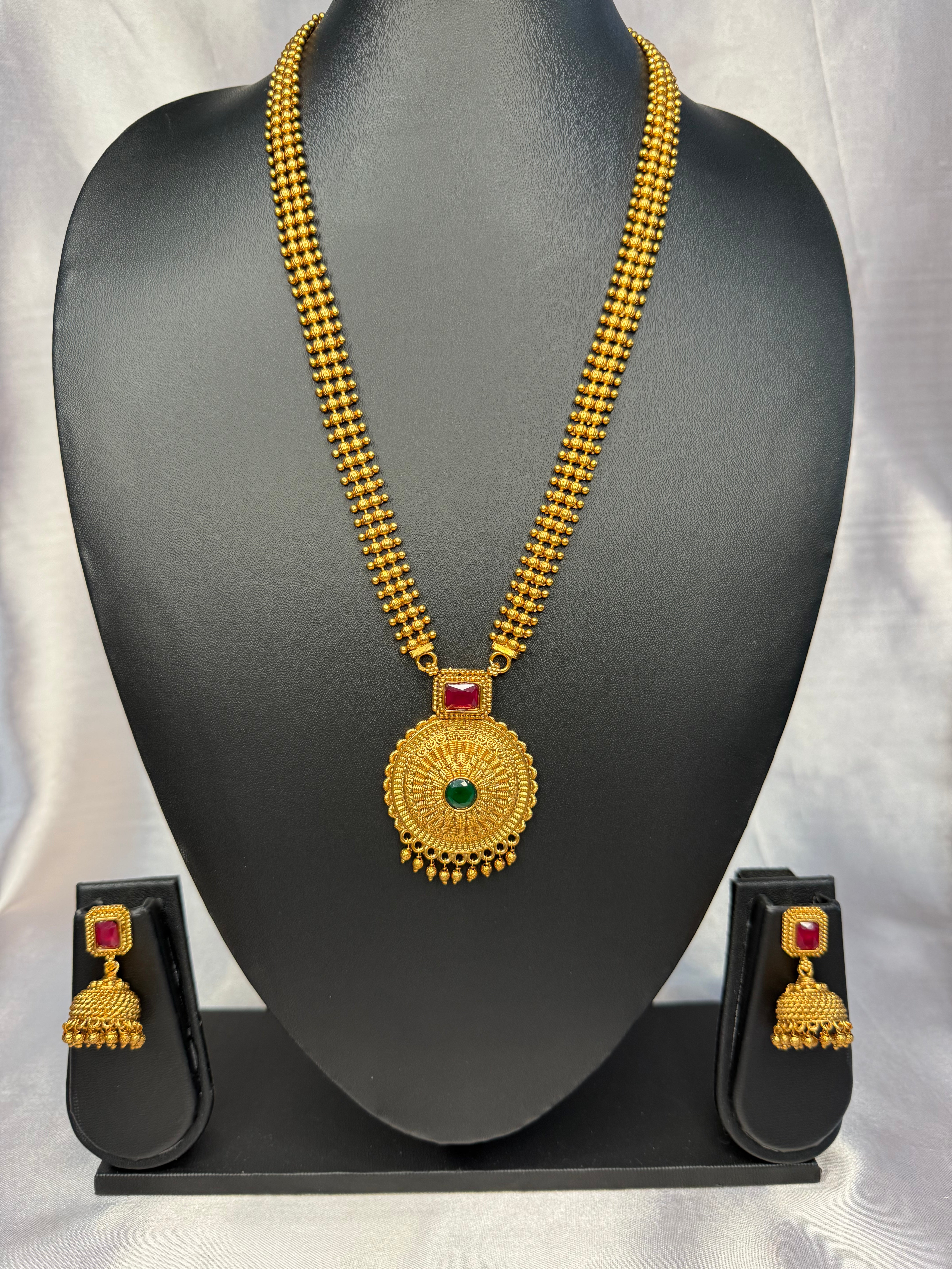 Gold necklace with pendant and earrings on a black mannequin bust against a white background