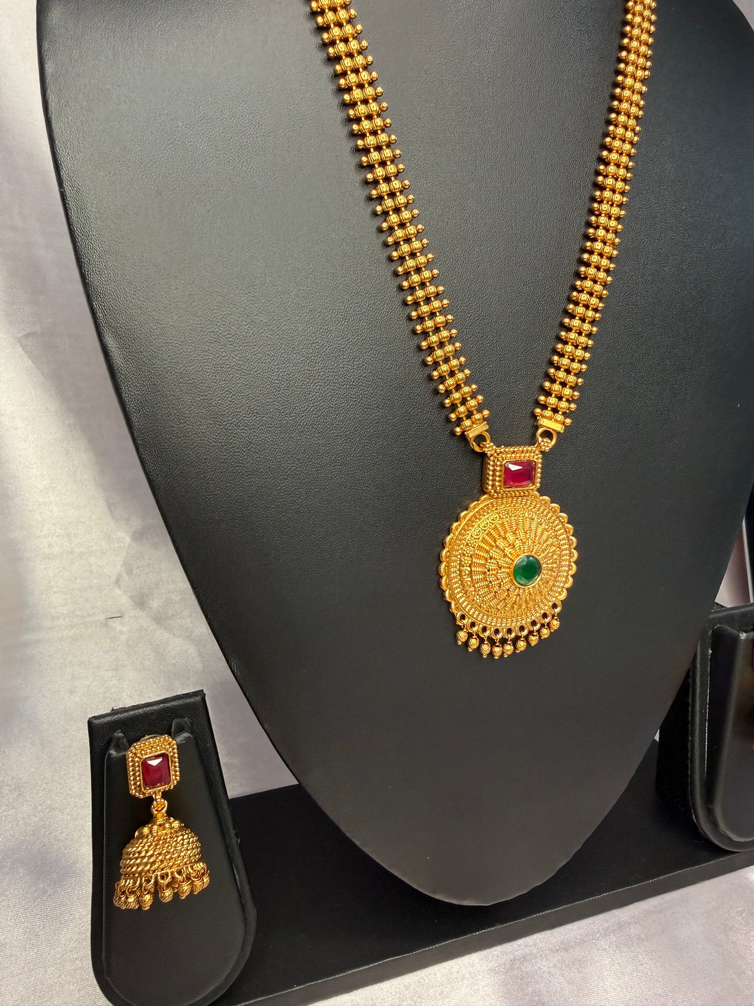 Gold necklace with pendant and earrings on a black mannequin bust against a white background