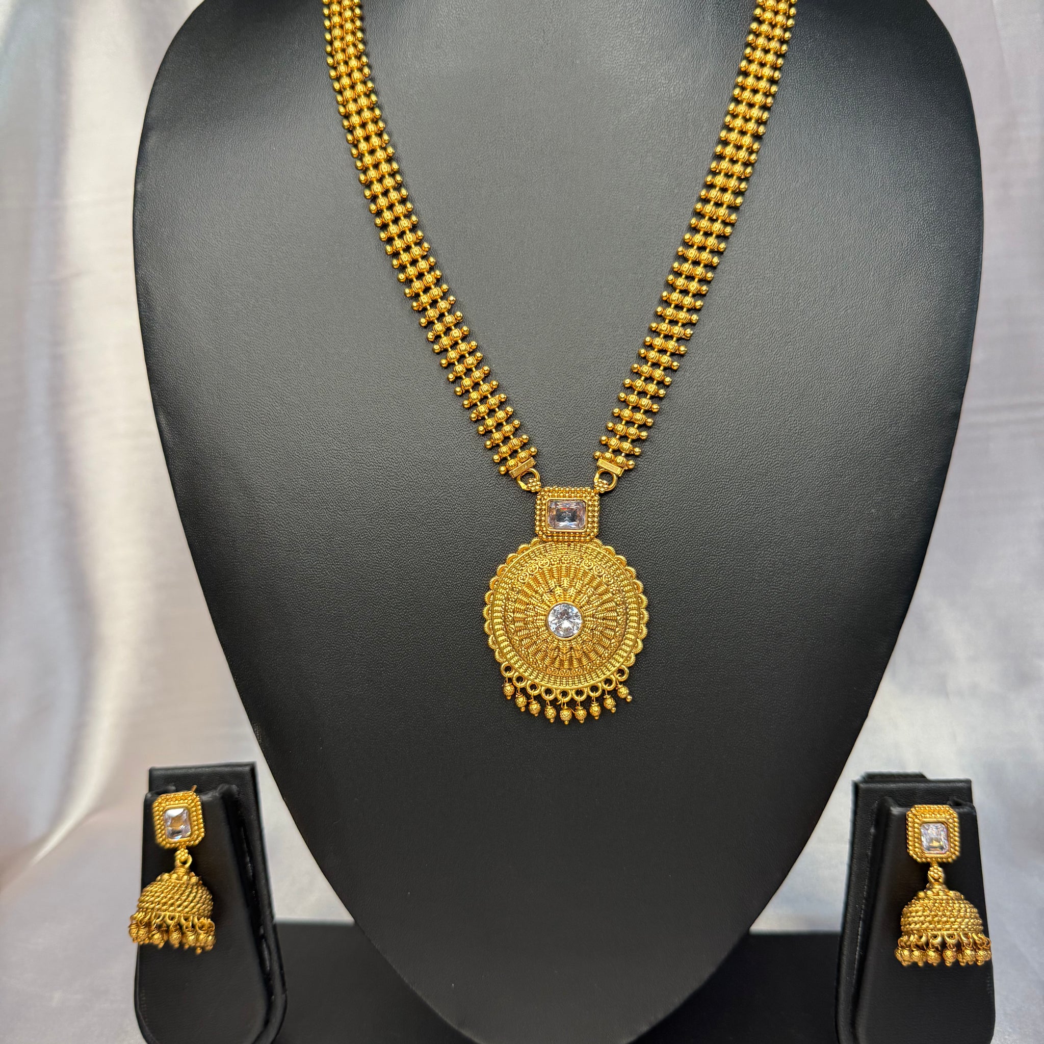Gold necklace and earrings set on a black mannequin bust with a gray background