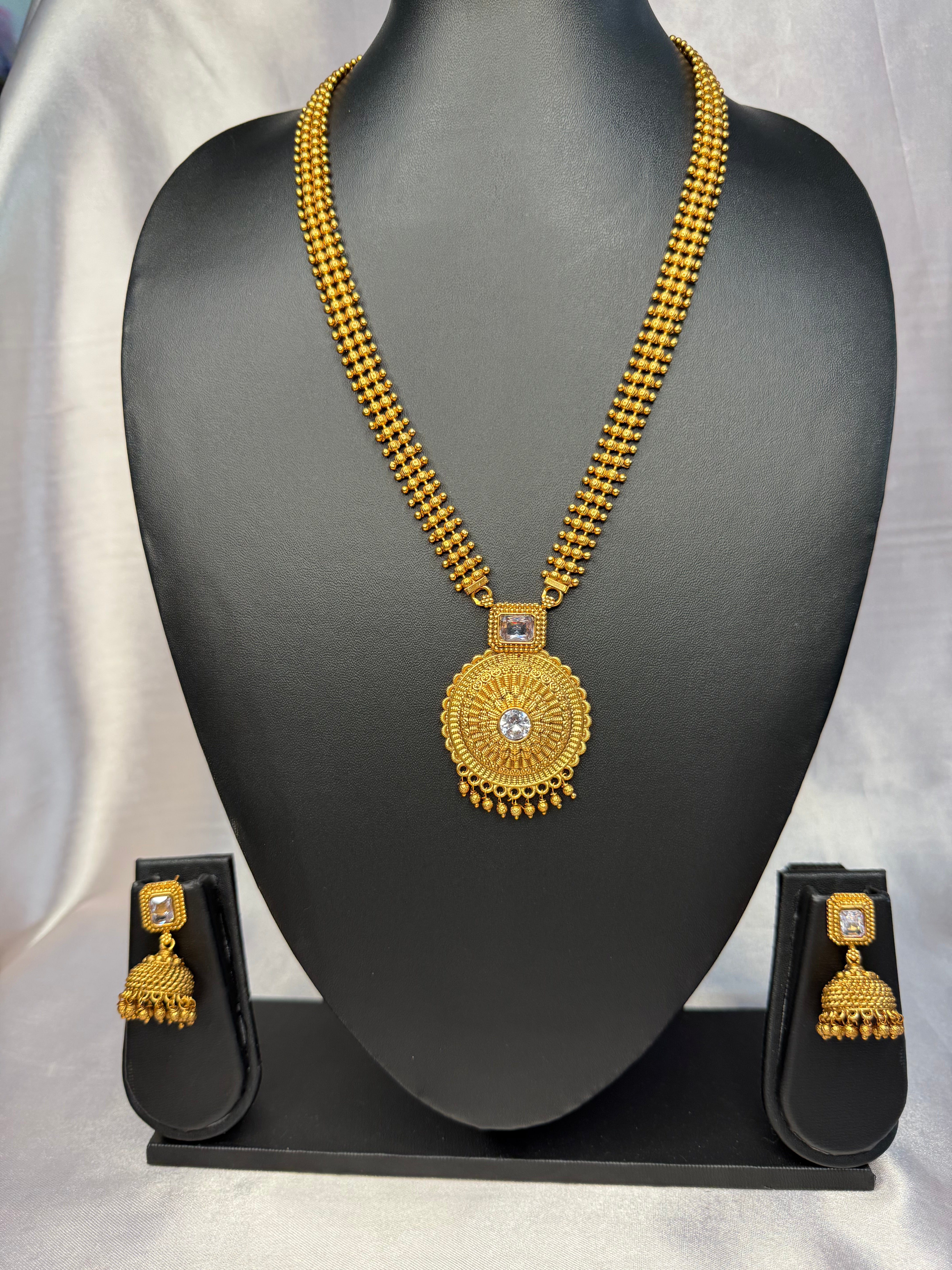 Gold necklace and earrings set on a black mannequin bust with a gray background