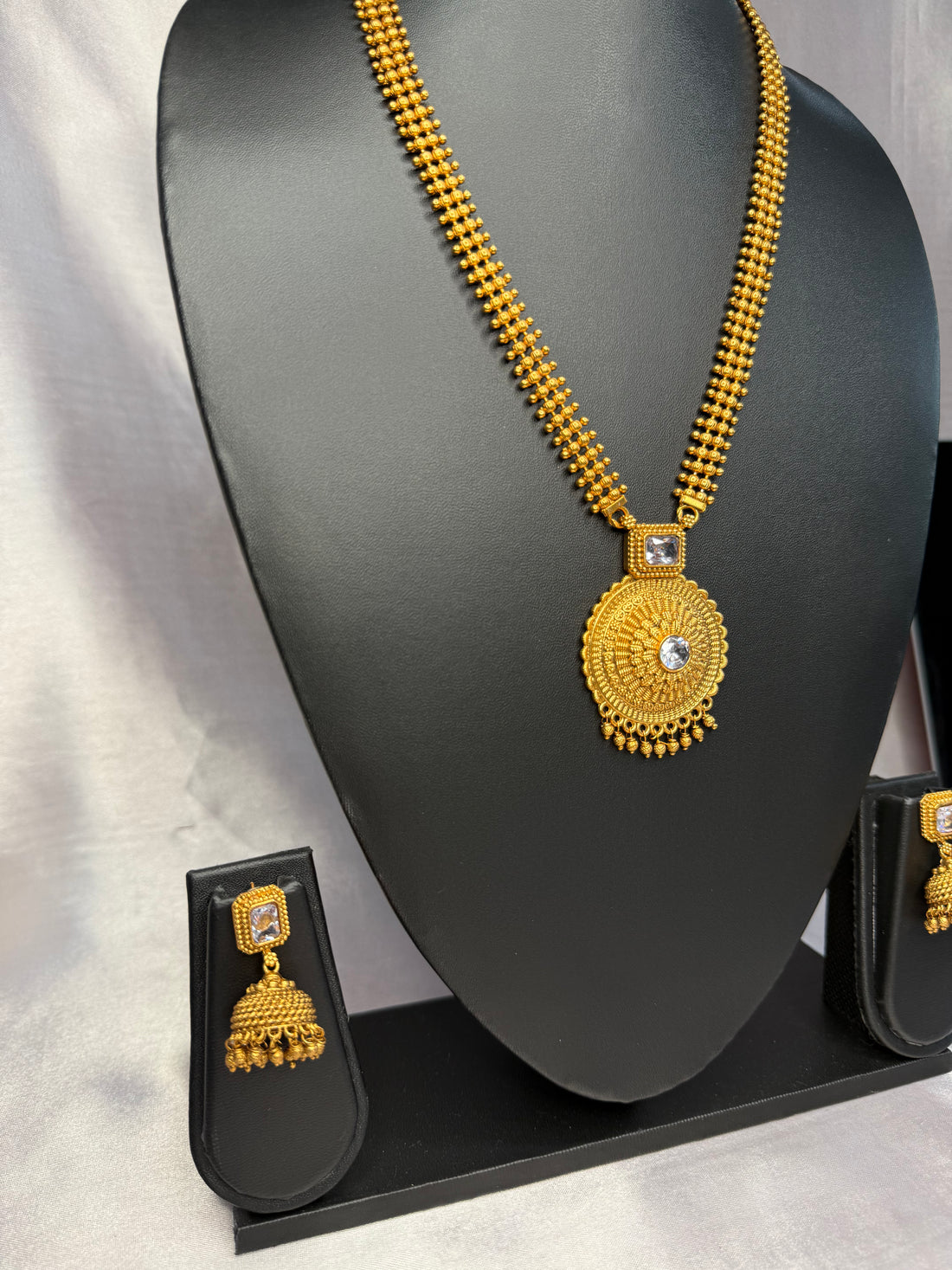 Gold necklace and earrings set on a black mannequin bust with a gray background