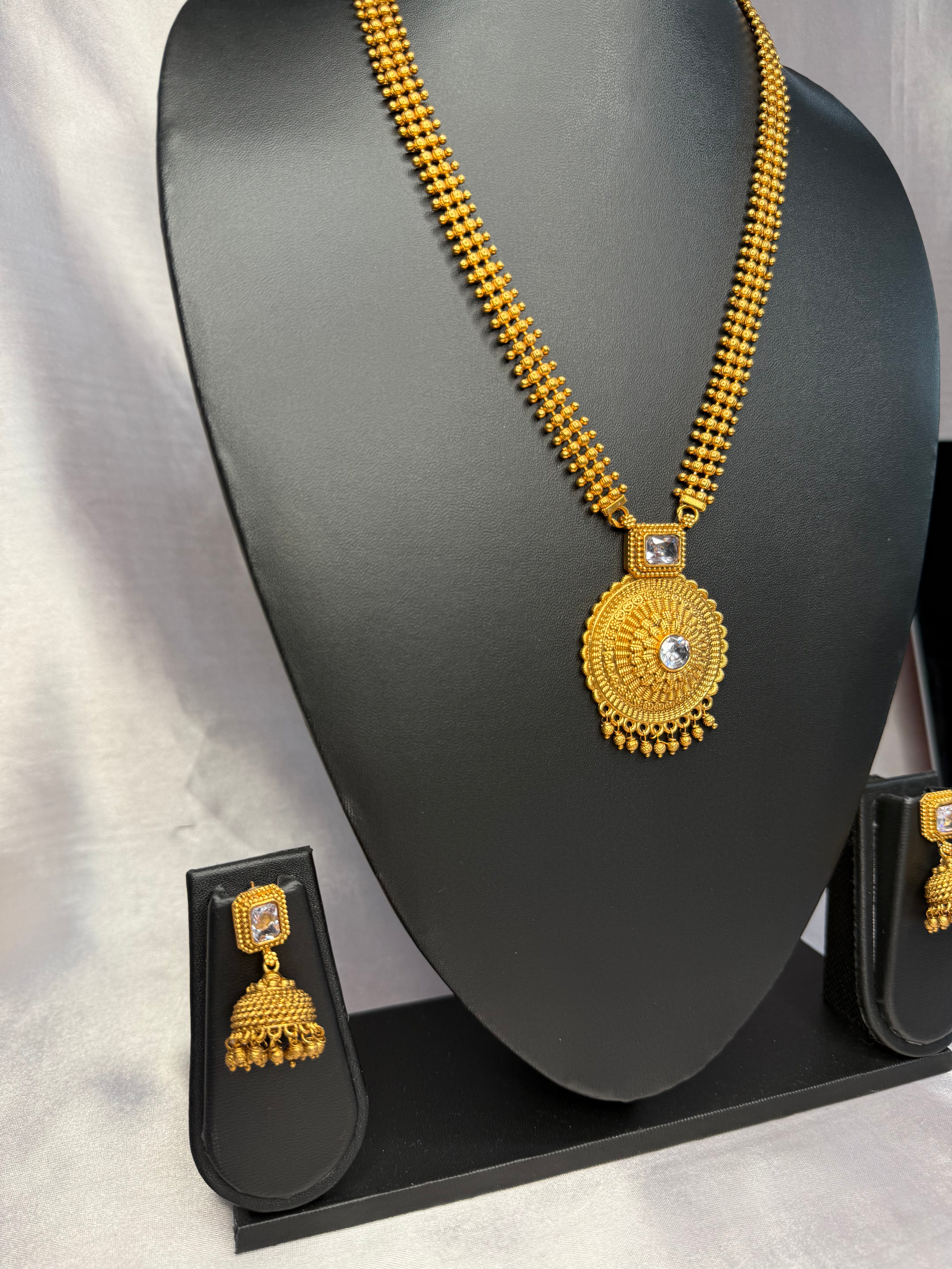 Gold necklace with pendant on a black stand against a gray background