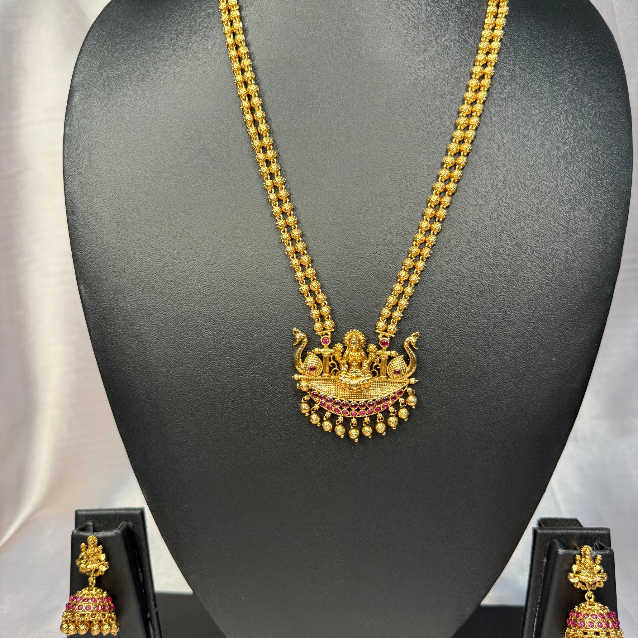 Gold necklace with a pendant and matching earrings on a black mannequin bust.