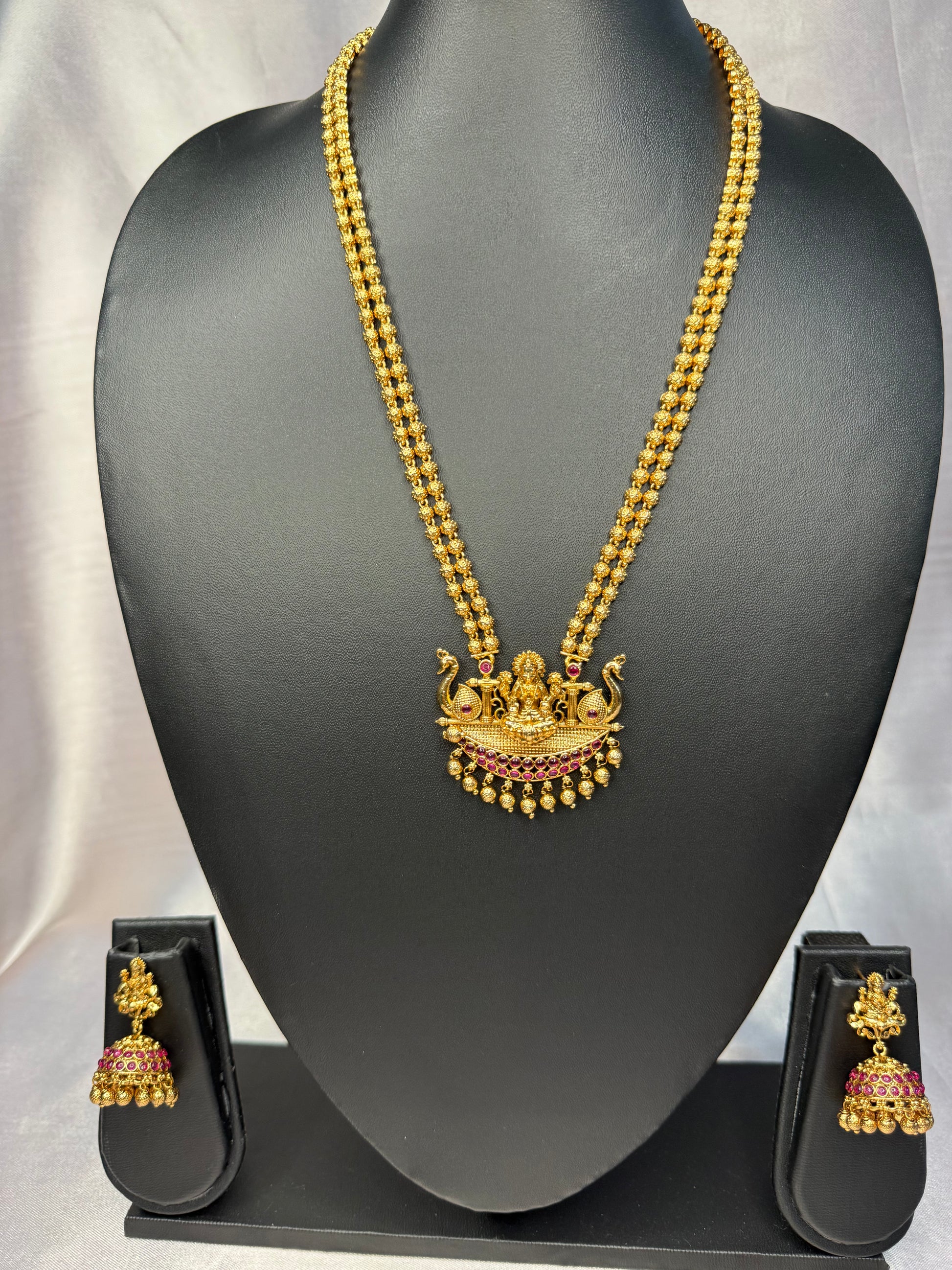Gold necklace with a pendant and matching earrings on a black mannequin bust.