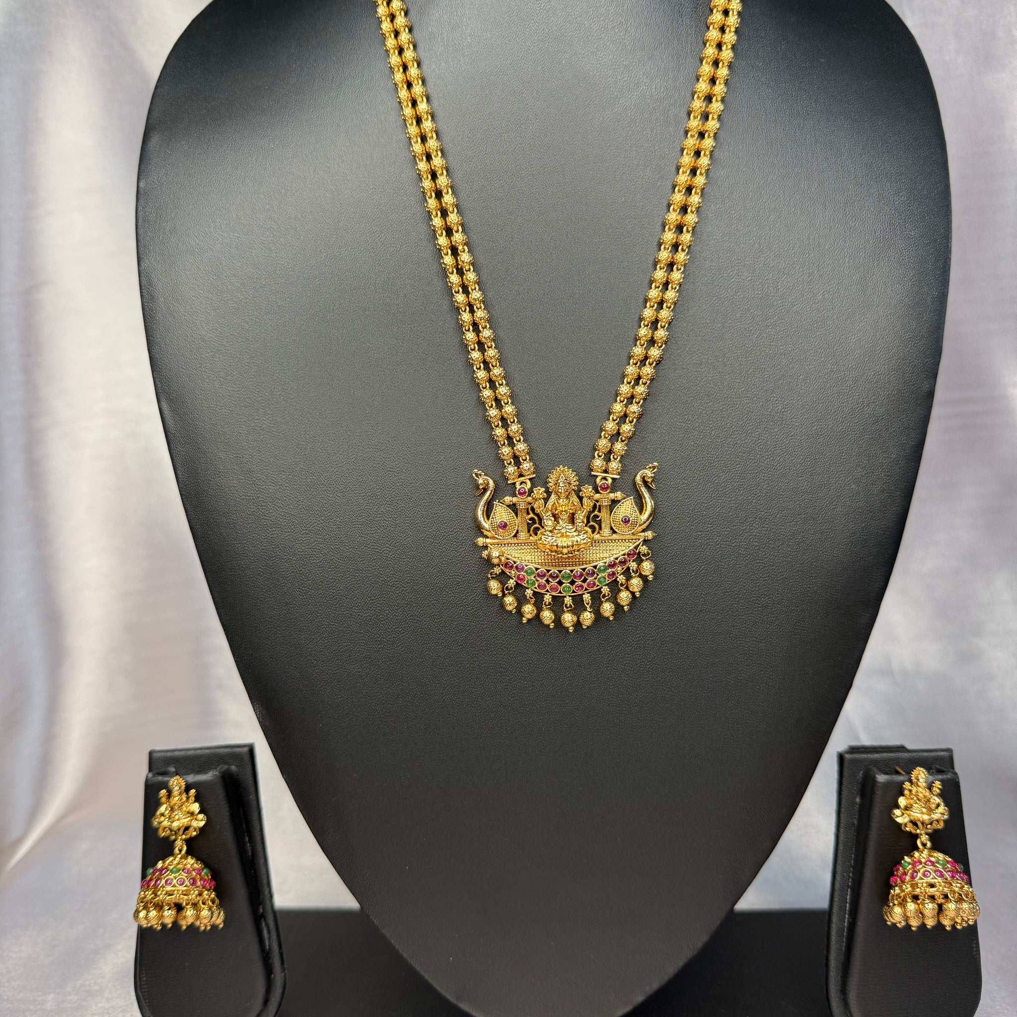 Gold necklace and earrings set on a black mannequin with a gray background