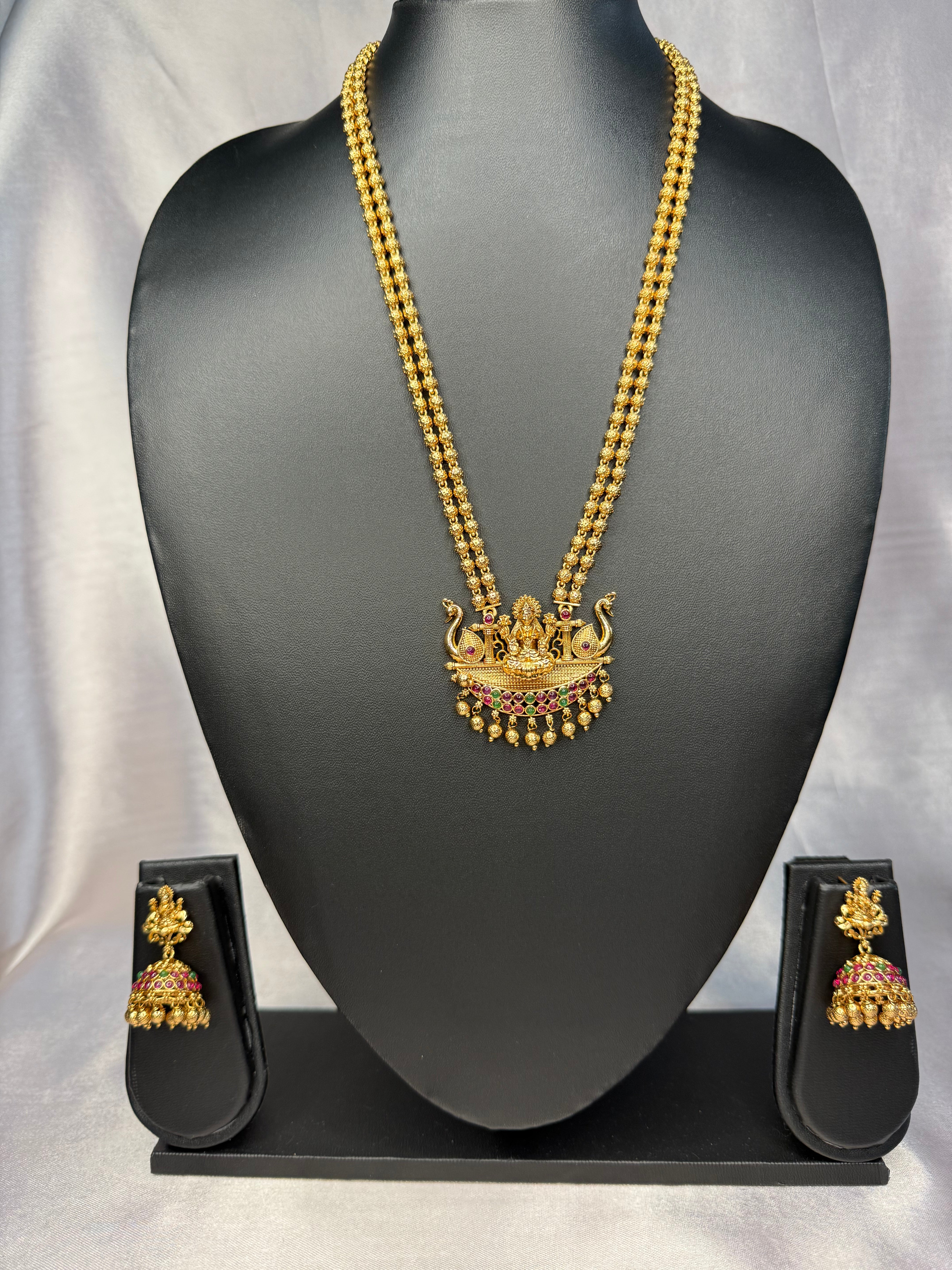Gold necklace and earrings set on a black mannequin with a gray background