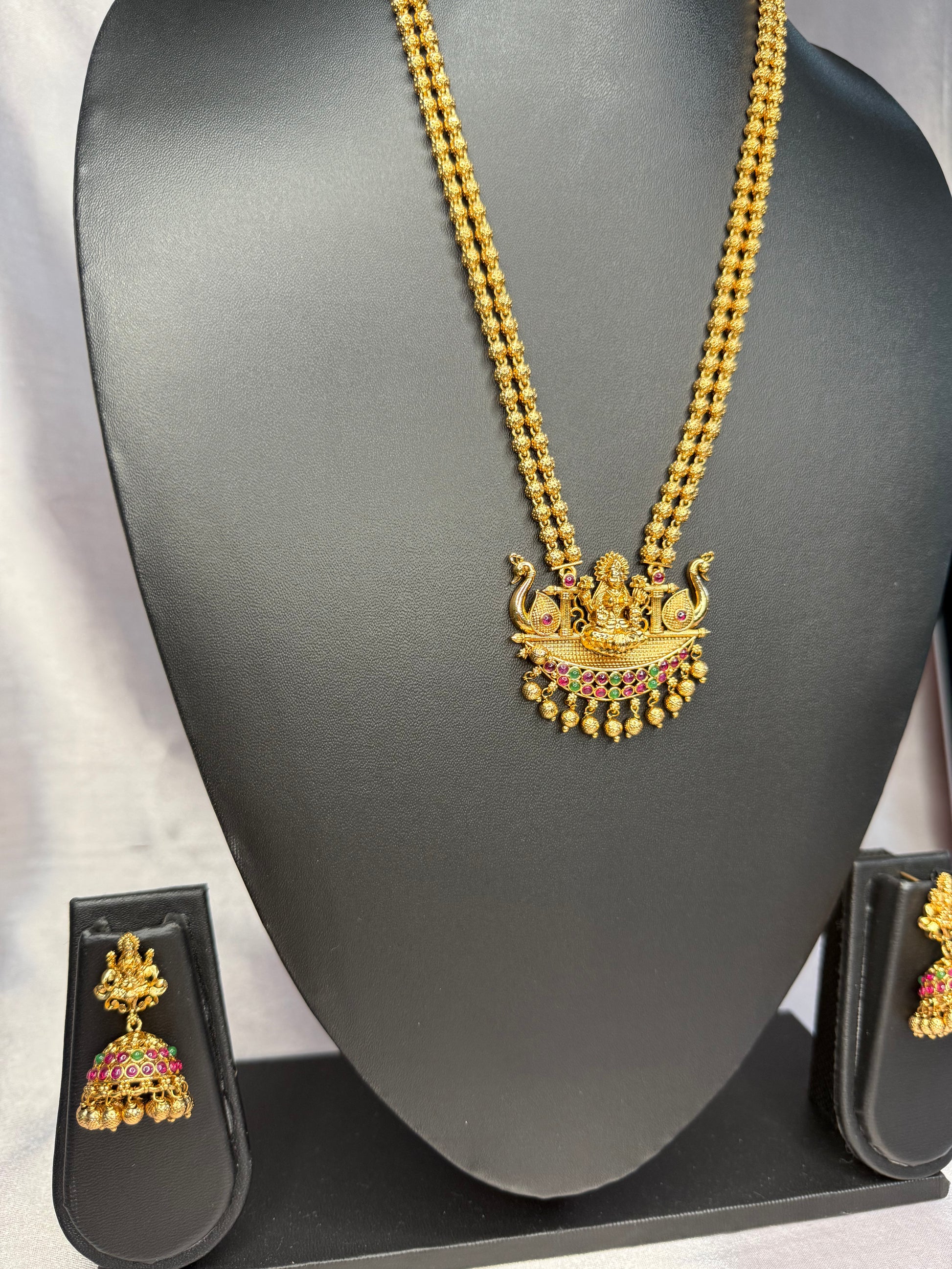 Gold necklace with a pendant on a black mannequin bust, accompanied by matching earrings.