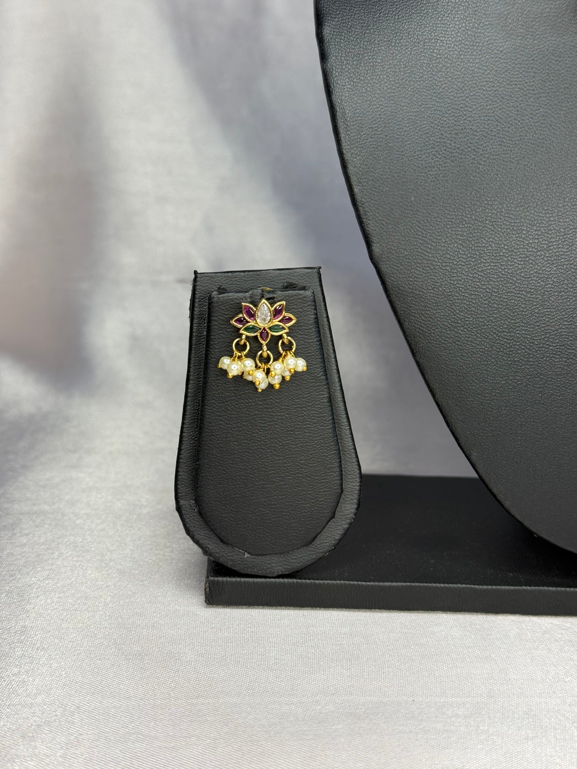 Gold and pearl earring on a black stand with a gray background