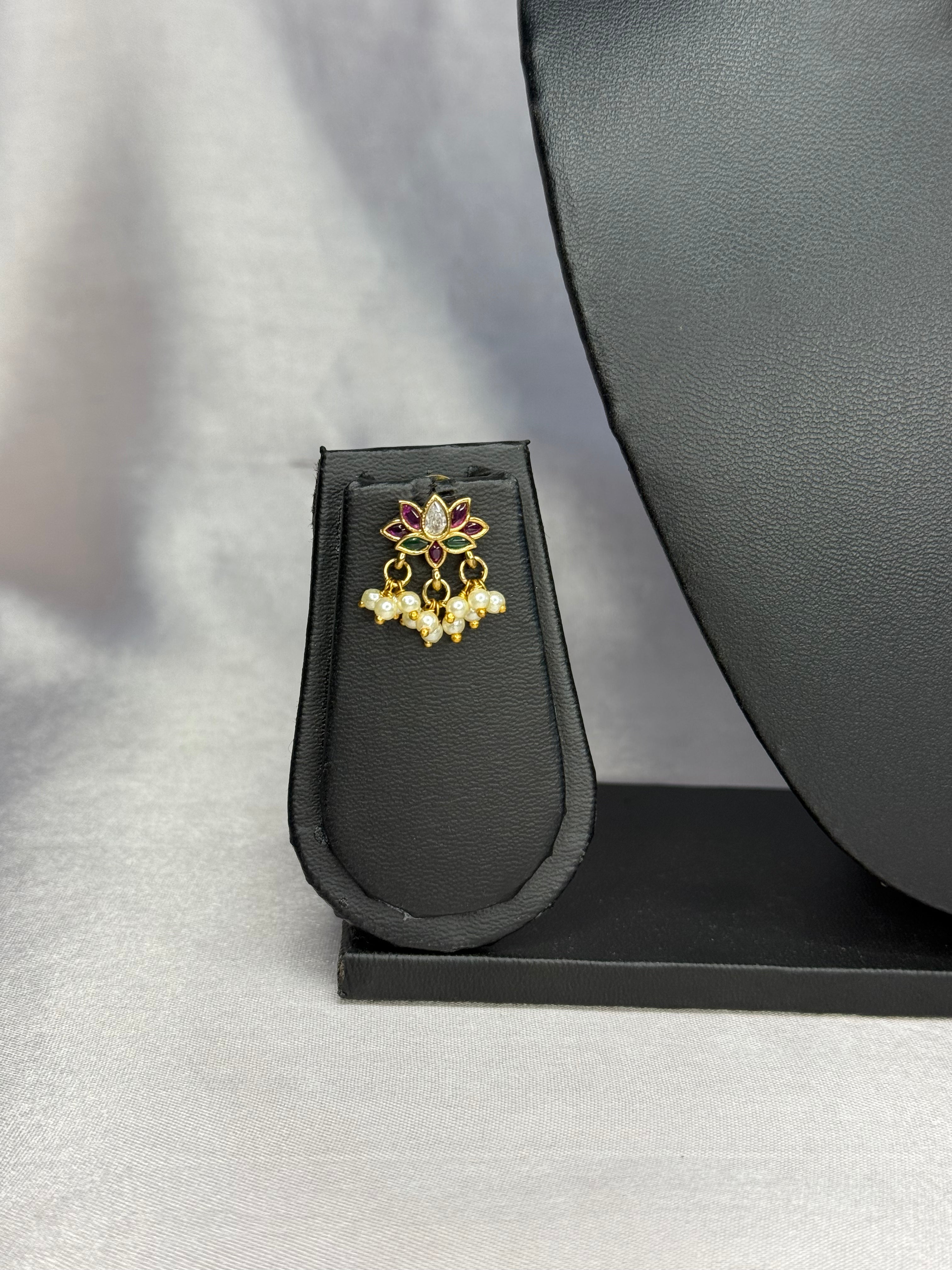 Gold and pearl earring on a black stand with a gray background