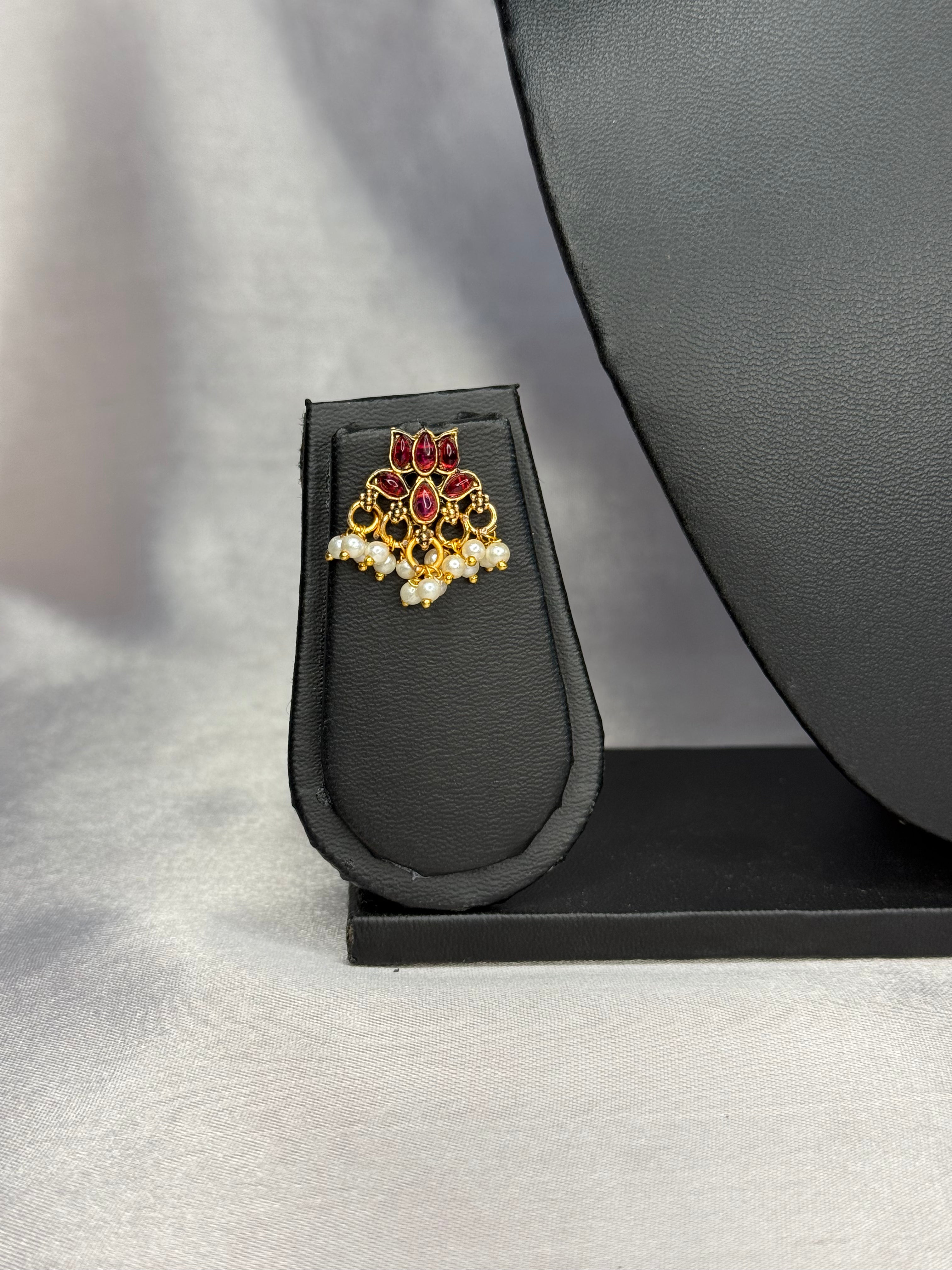 Jewelry box with a decorative brooch featuring red and gold elements on a gray background.