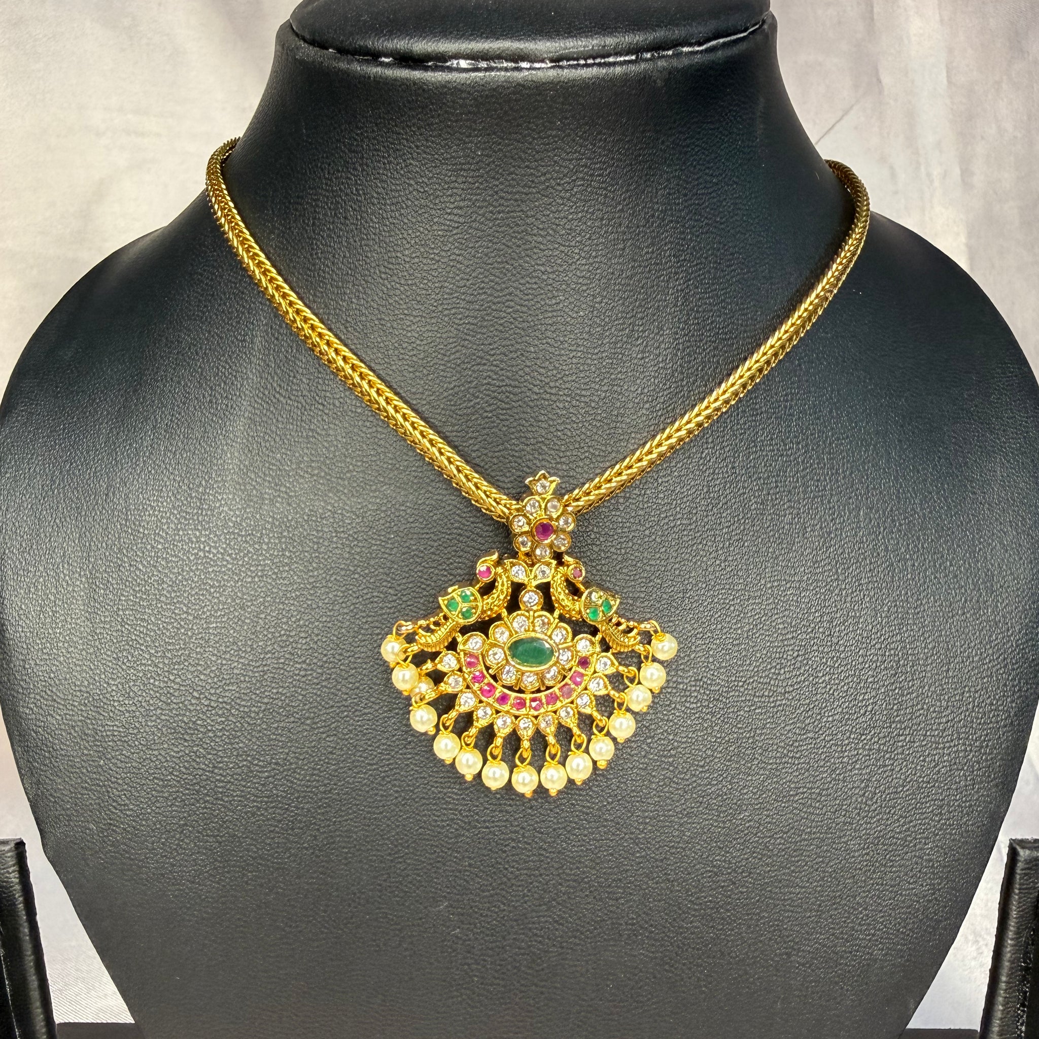 Gold necklace with a decorative pendant on a black mannequin bust.