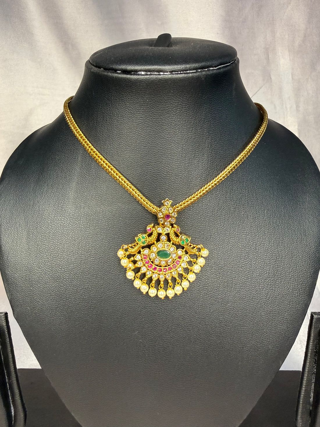 Gold necklace with a decorative pendant on a black mannequin bust.