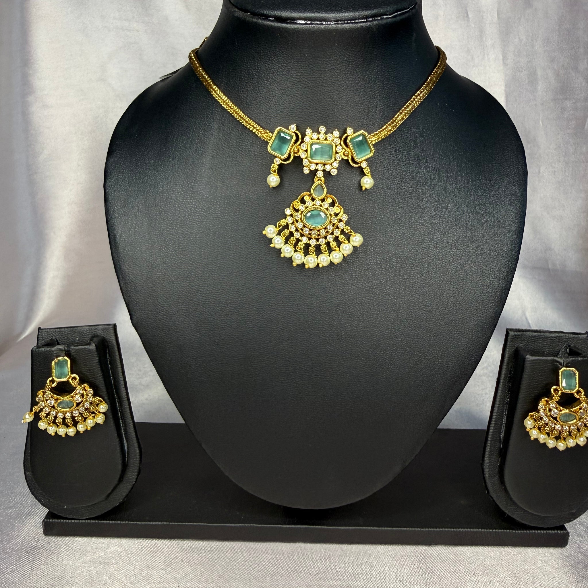 Gold and green jewelry set on a black mannequin bust with a plain background