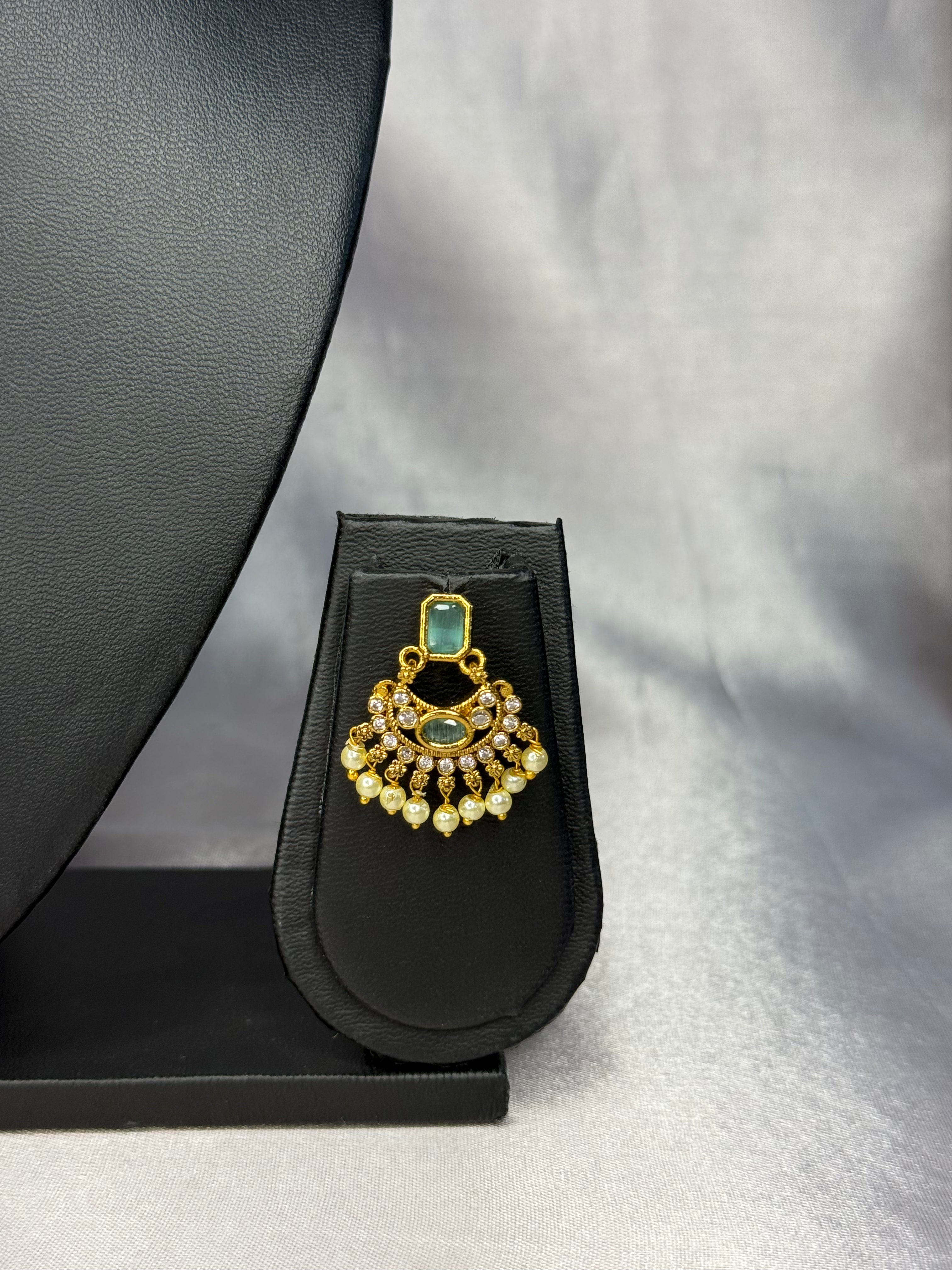 Gold and green gemstone necklace on a black stand against a gray background