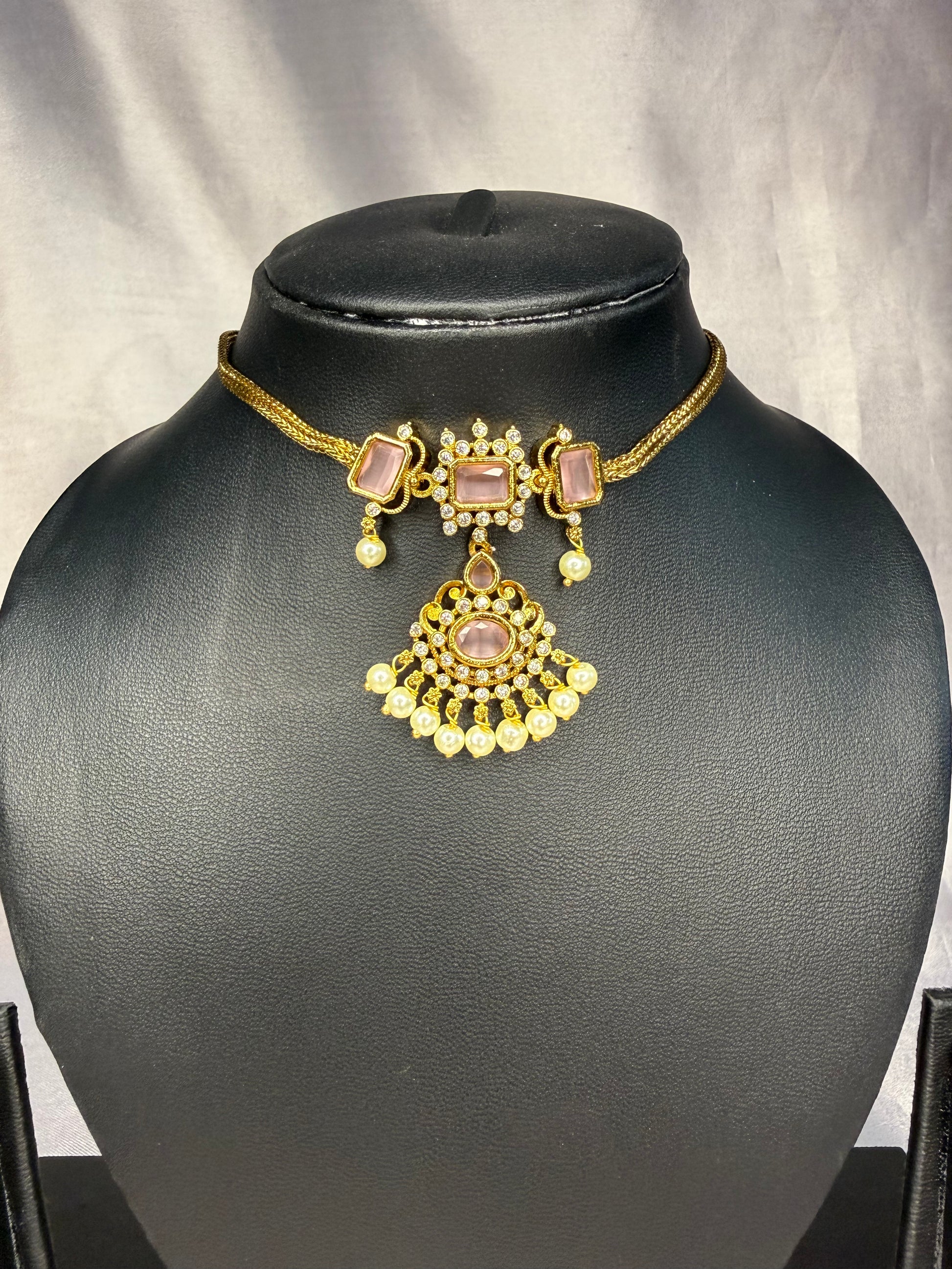 Gold necklace with pink stones on a black mannequin bust against a gray background