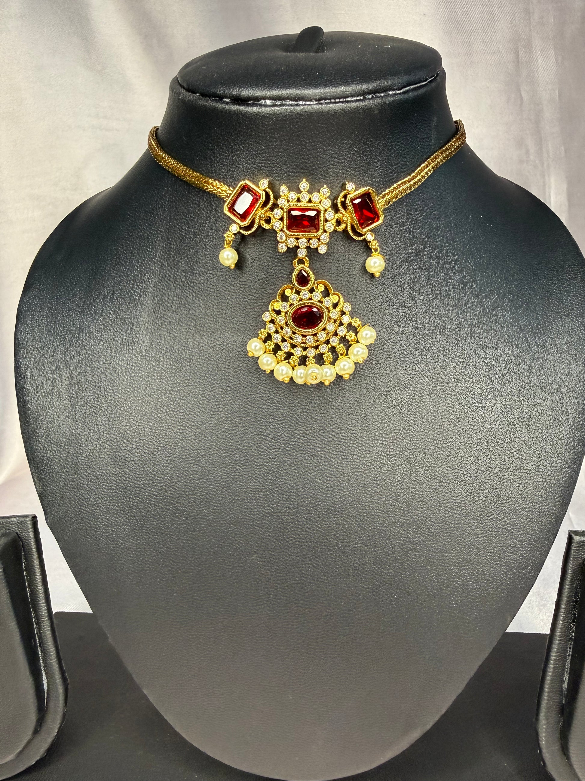 Gold necklace with red gemstones on a black mannequin bust against a gray background
