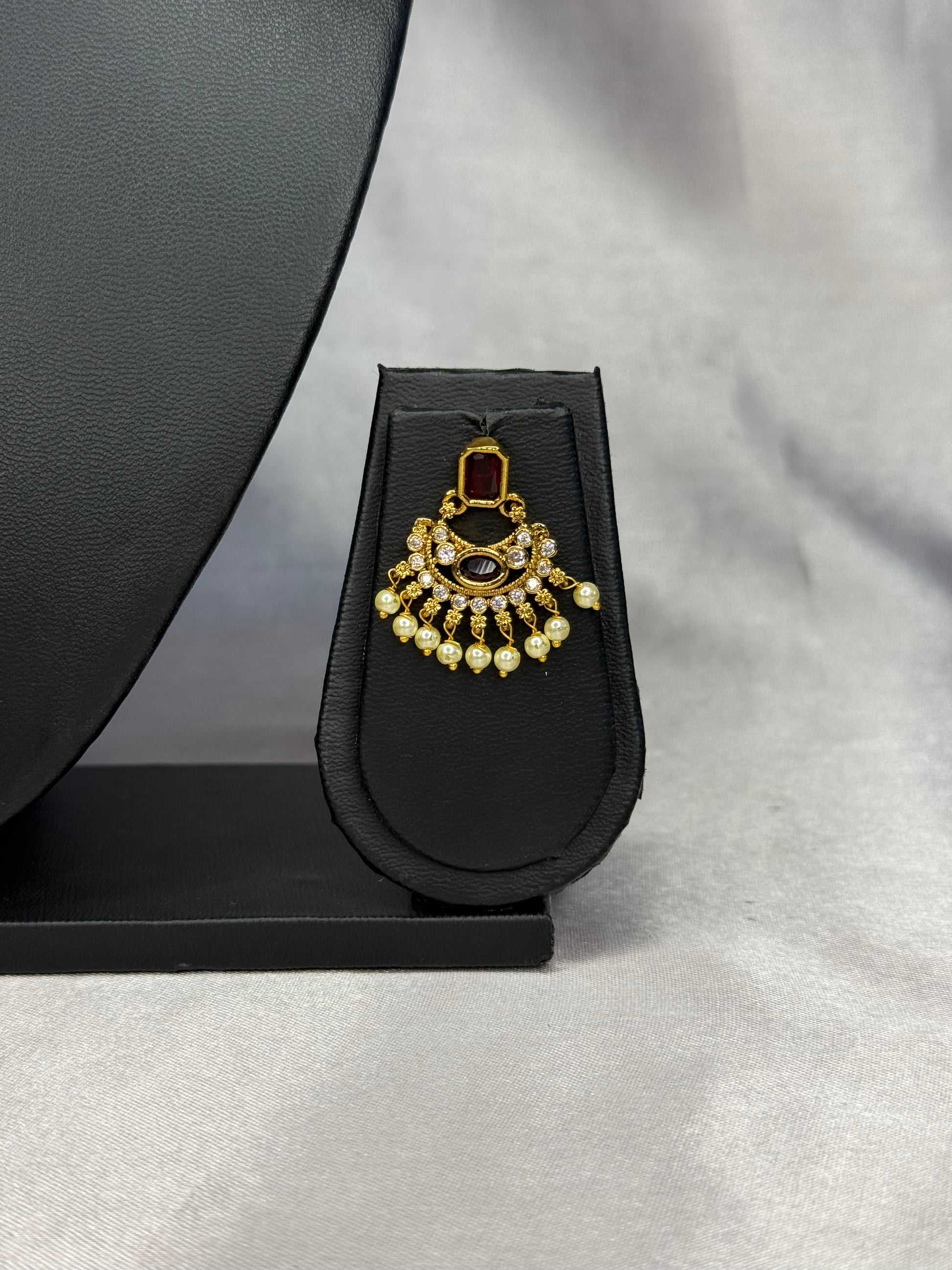 Decorative earring on a black stand against a gray background