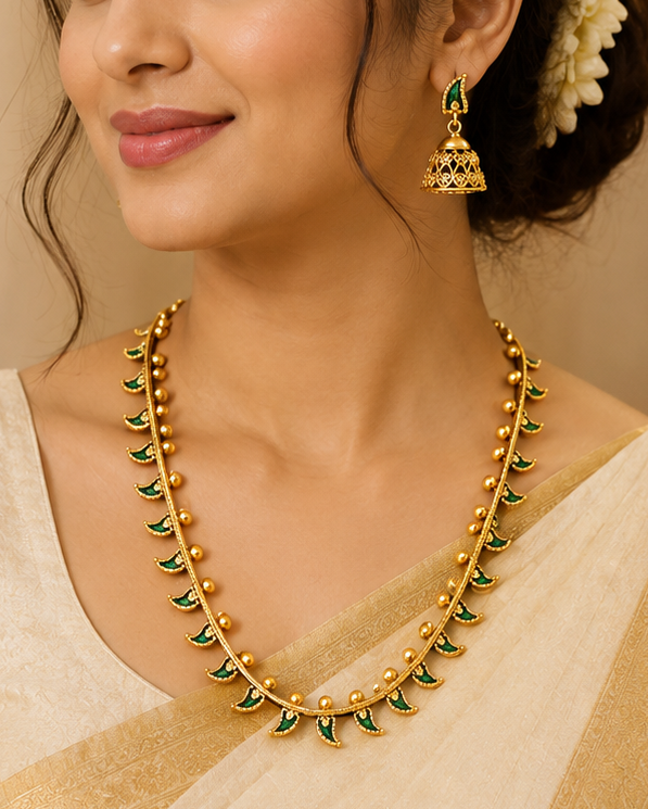 A woman wearing a cream-colored sari with gold borders and a matching gold necklace with green stone accents, styled with a white flower in her hair.
